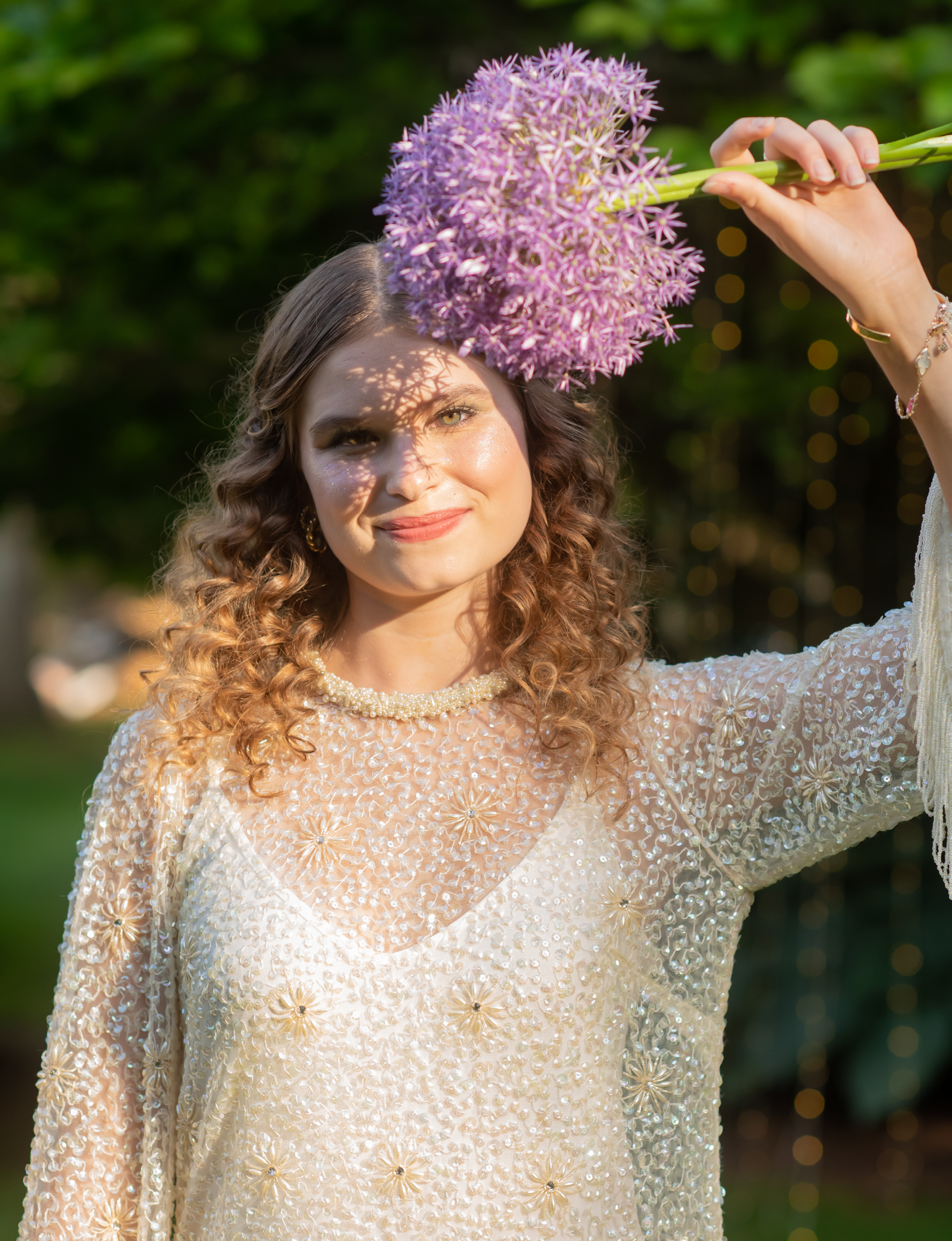 girl wearing a beaded and floral pearl dress holding a large purple allium flower