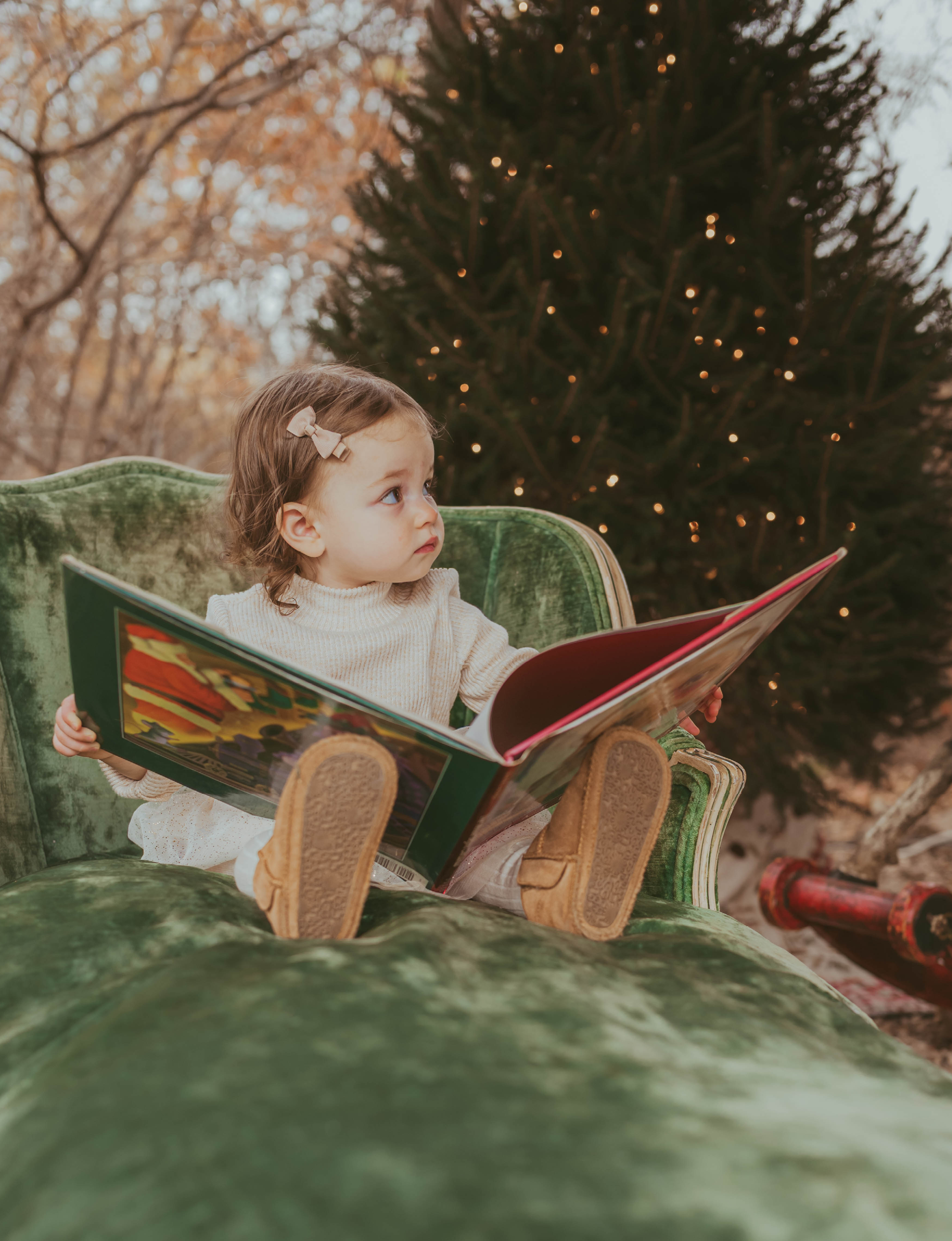 Child reading large book with Christmas tree