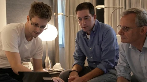 Still from Laura Poitras’s “Citizenfour” (2014). From left to right, Edward Snowden, Glenn Greenwald, and reporter Ewen MacAskell, all surrounded around a computer containing the leaked NSA files. Courtesy of HBO Films, Participant Media, and Praxis Films.