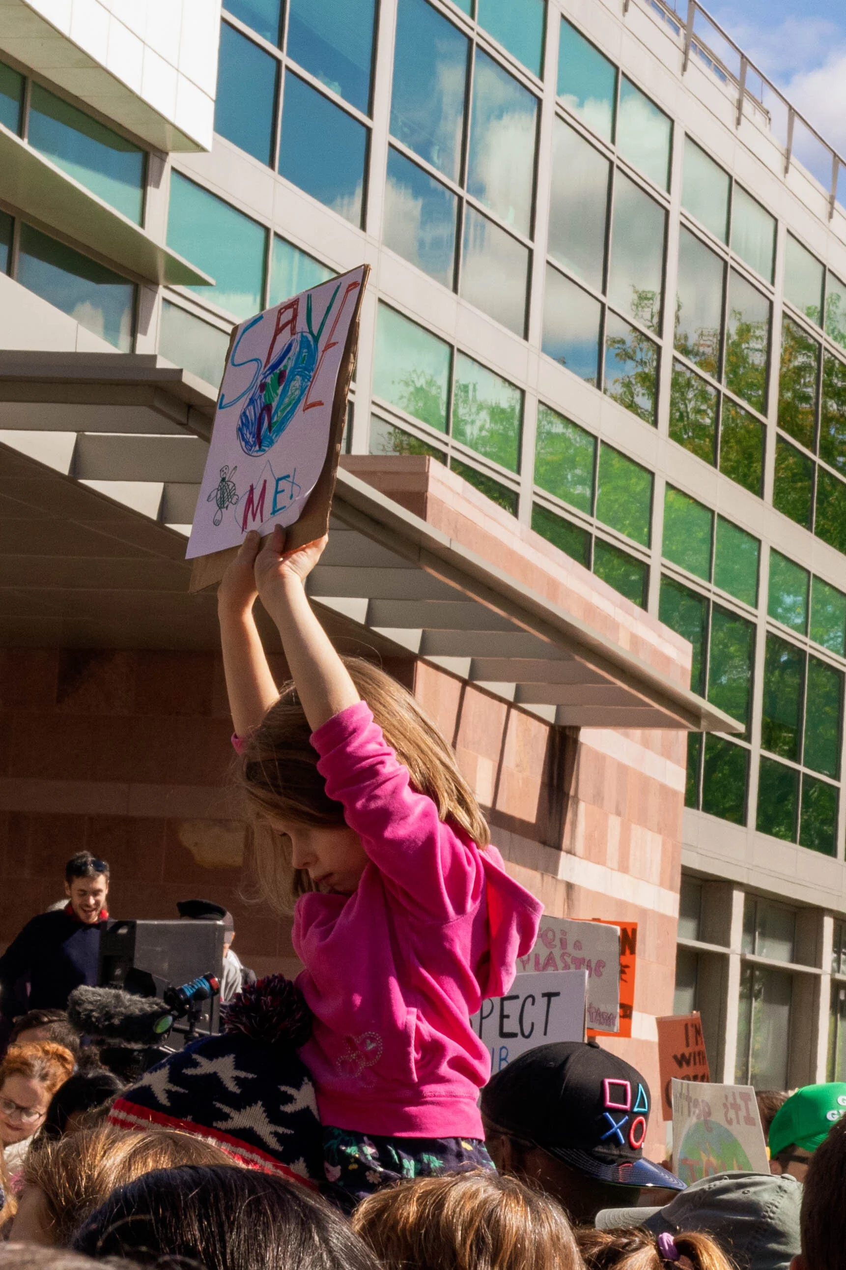 A child holds a hand-drawn sign, demanding the world be saved. Photo by Hayley Anderson