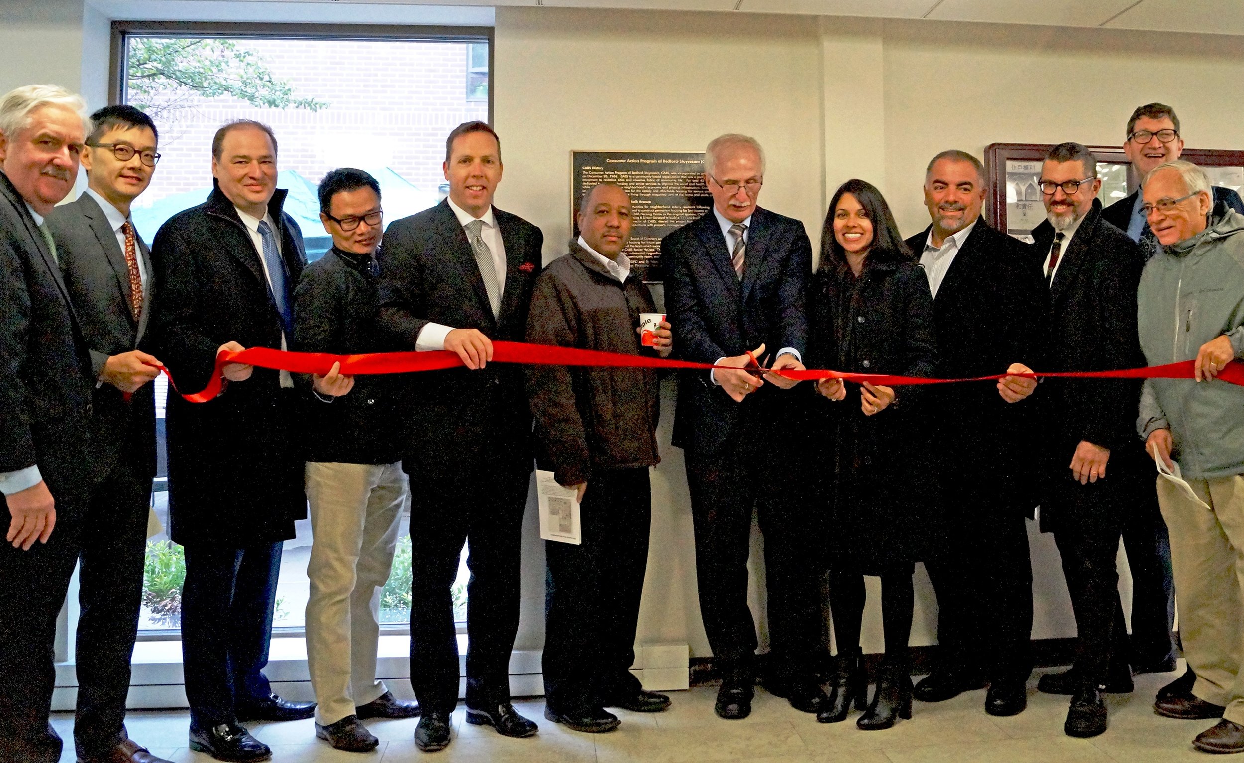 William Pernisek (center) does the honors at the ribbon cutting to rededicate CABS Senior Housing. Also present (l to r) Michael Rochford, Exec. Dir. St. Nicks Alliance; Terence Tsang, New York State Homes and Community Renewal; Charlie Georgelis, FG-PH Corp.; Tian Chen, FG-PH Corp.; Niall Murray – Rockabill; Carlos Cassius, FG-PH Corp.; Sharmi Sobhan, JP Morgan Chase; Joe Robles, SNA Board President; Damon Strub, Nomad Architecture; Frank Lang, St. Nicks Alliance’s Dir. of Housing; and David Dobosz, SNA Board Member