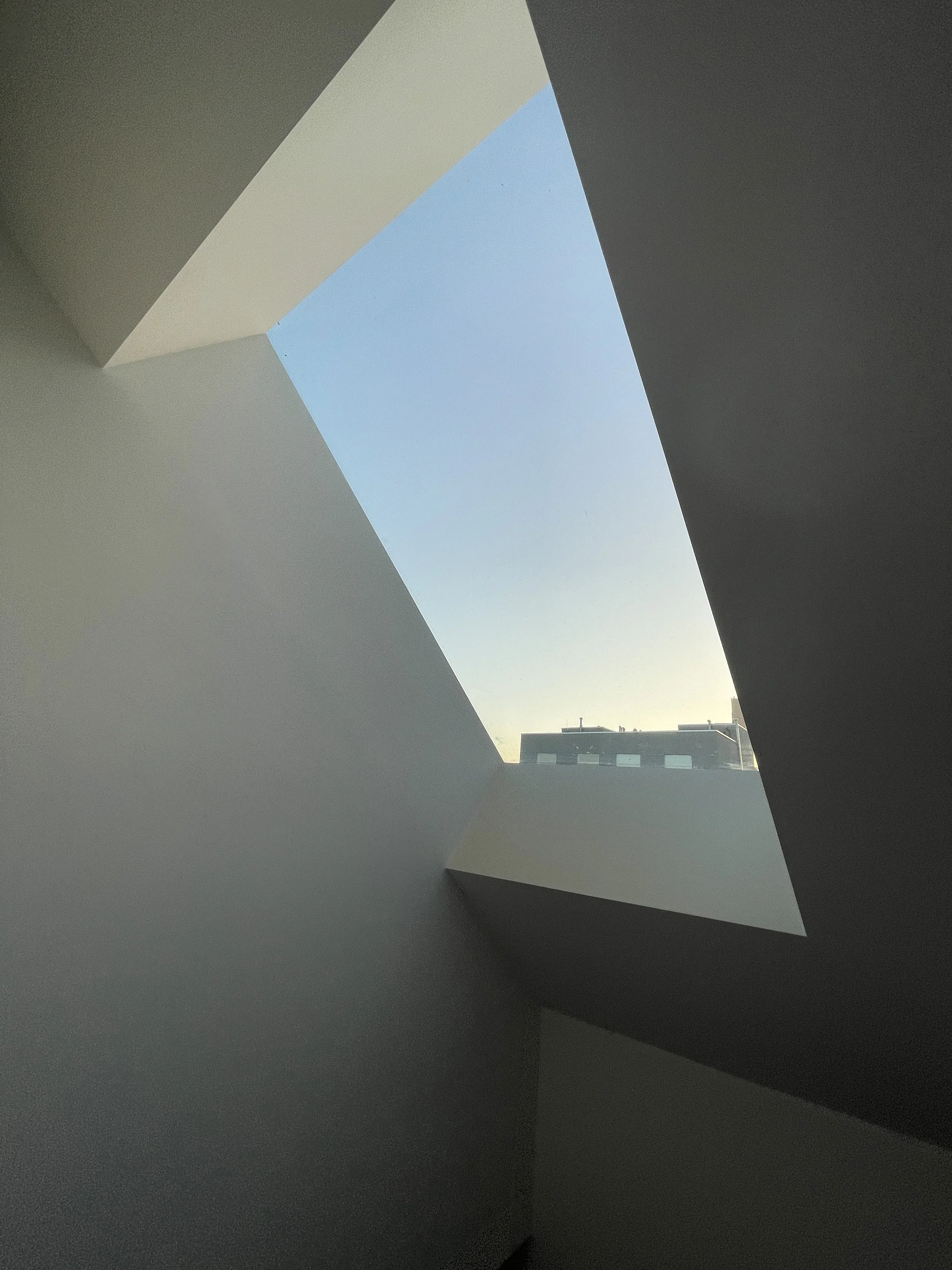 View of a ceiling skylight showing a clear blue sky and building rooftops.