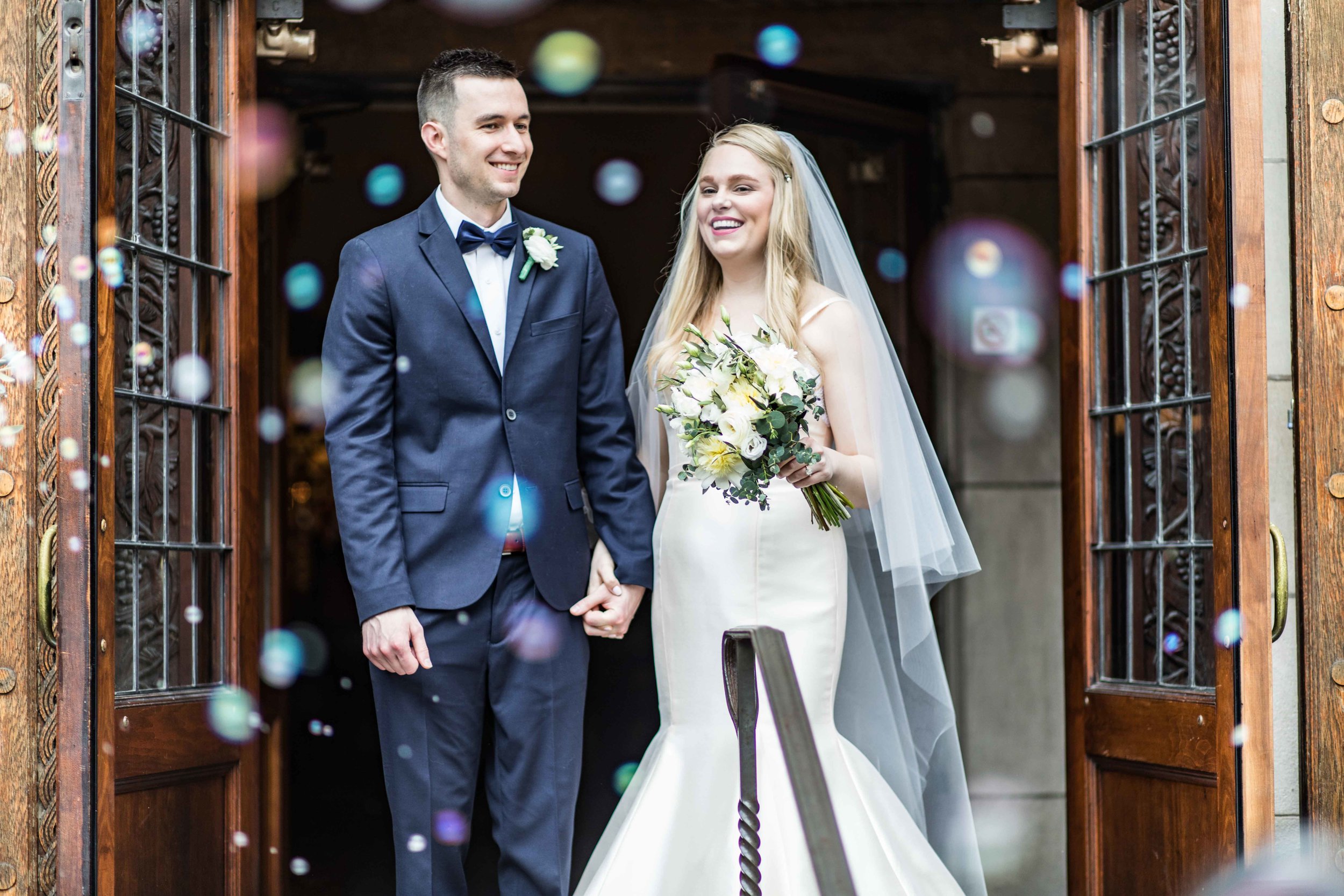  Bride and Groom bubble exit from the tall wood church doors 