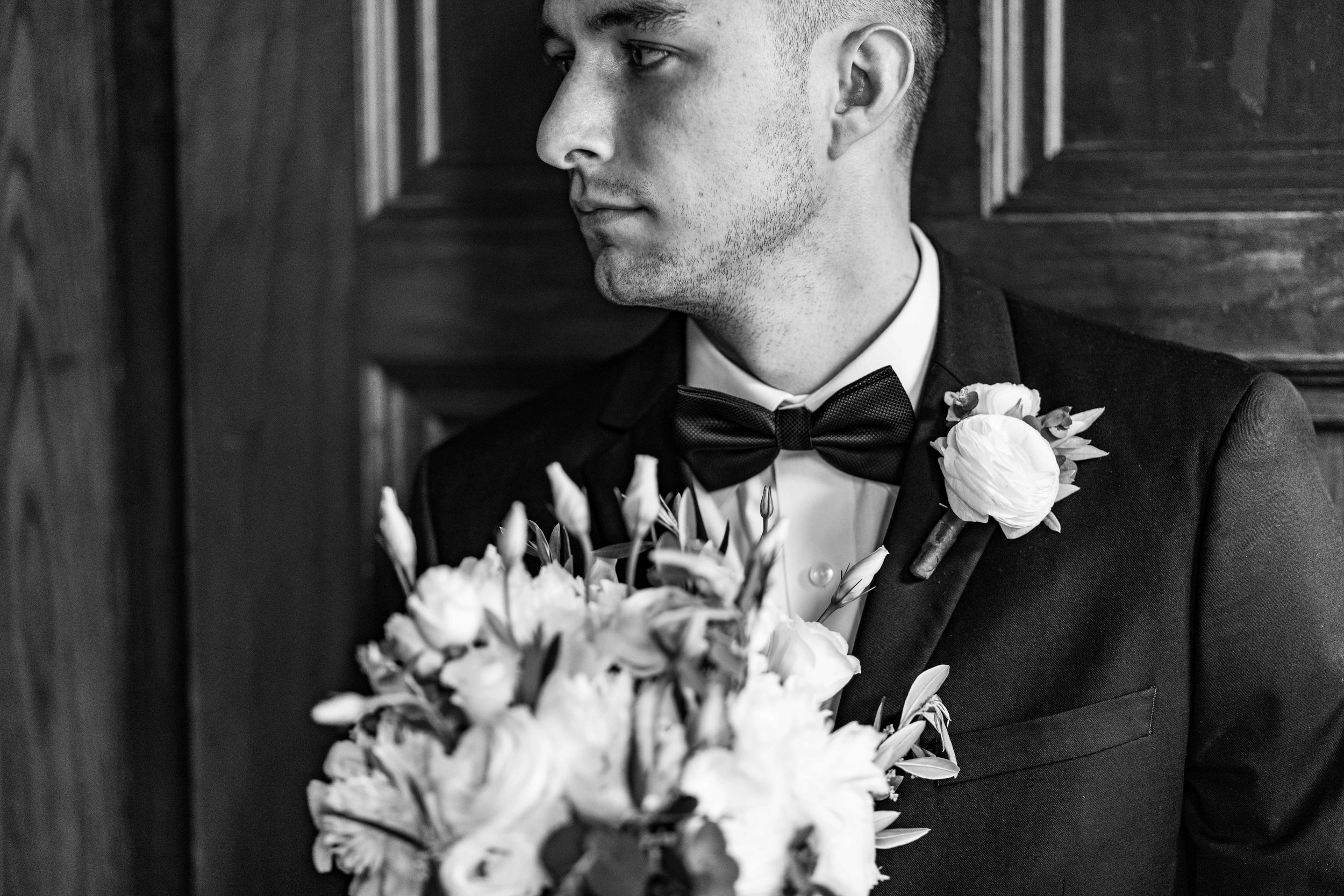  The Groom holding the brides bouquet against church door 