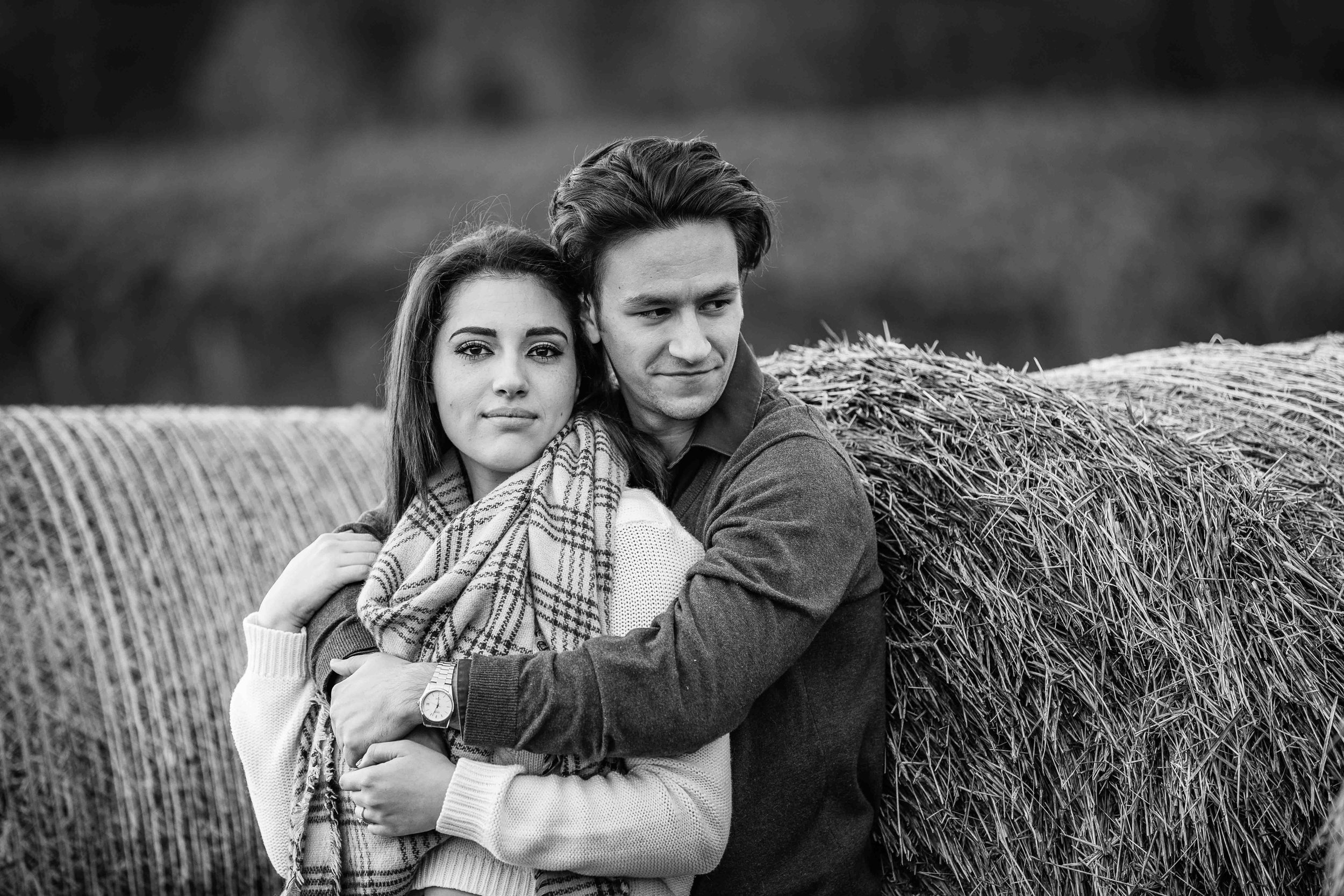  couple leaning on hay bale in field for engagement photos 