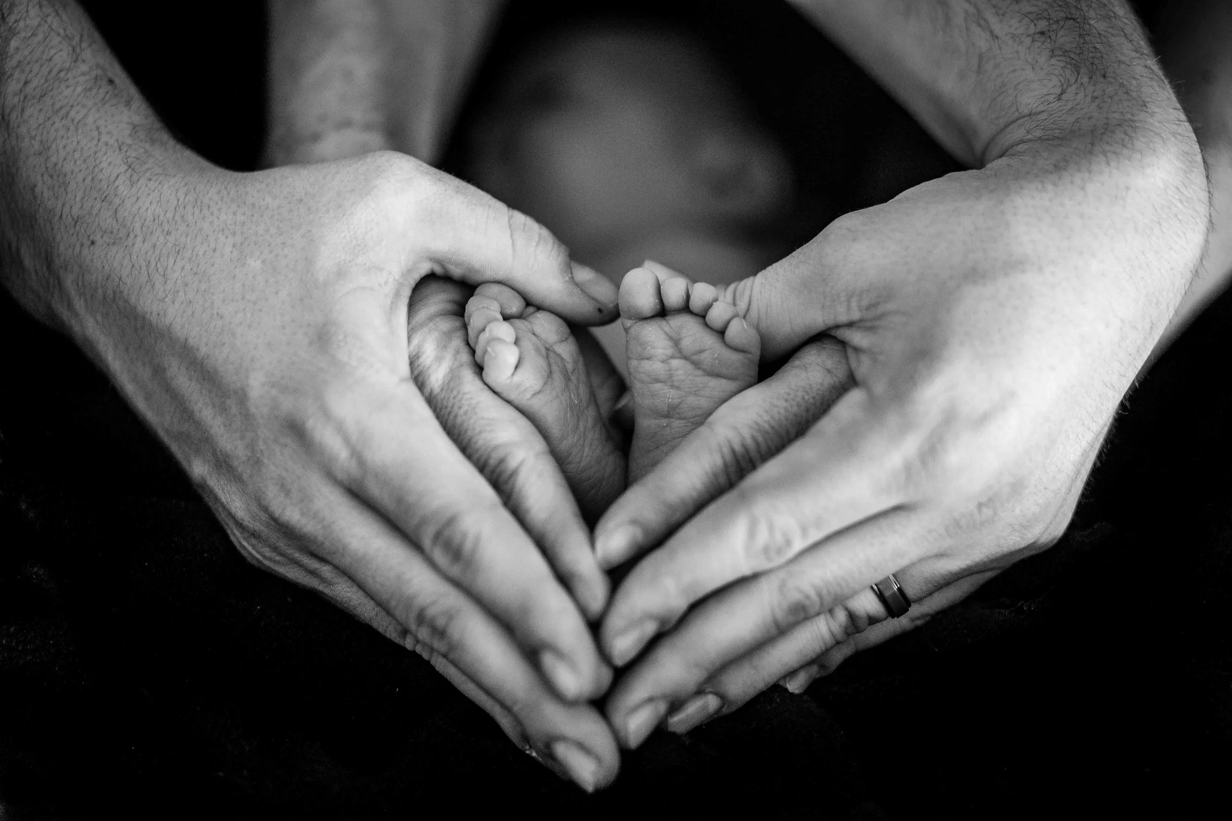 mother and father make a heart shape with their hands and baby’s feet