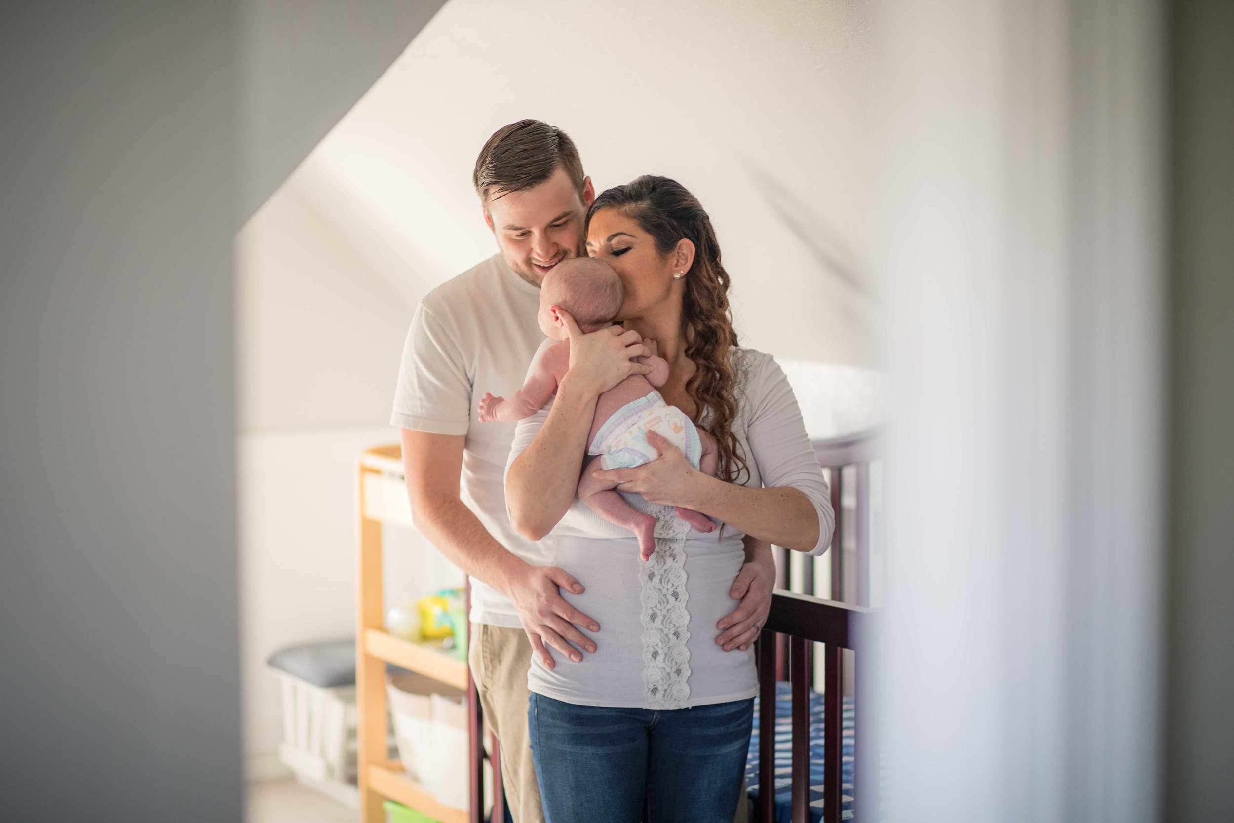  Dad holding mom as she kisses baby standing at their crib 