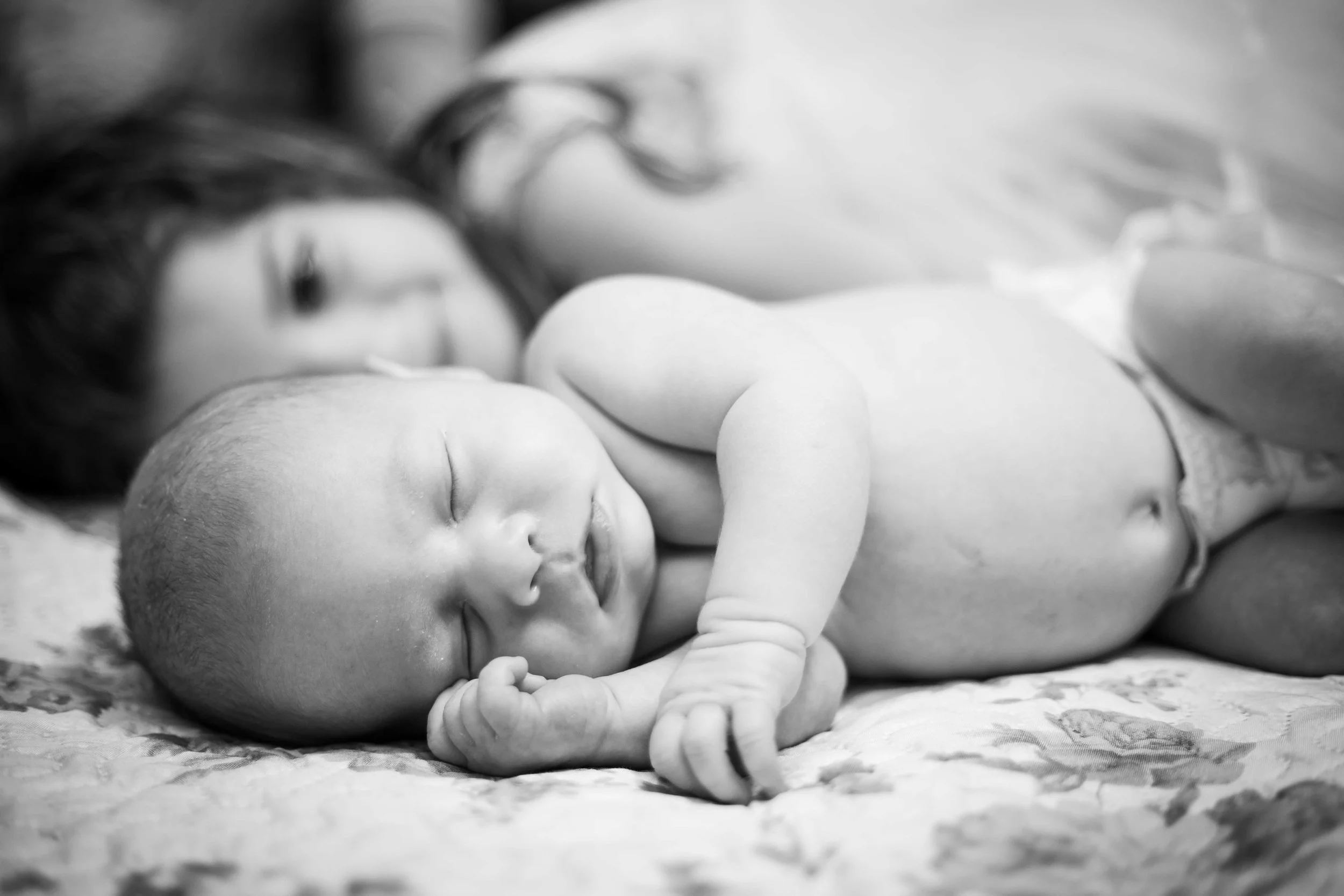 Newborn sleeping next to big sister on the family bed
