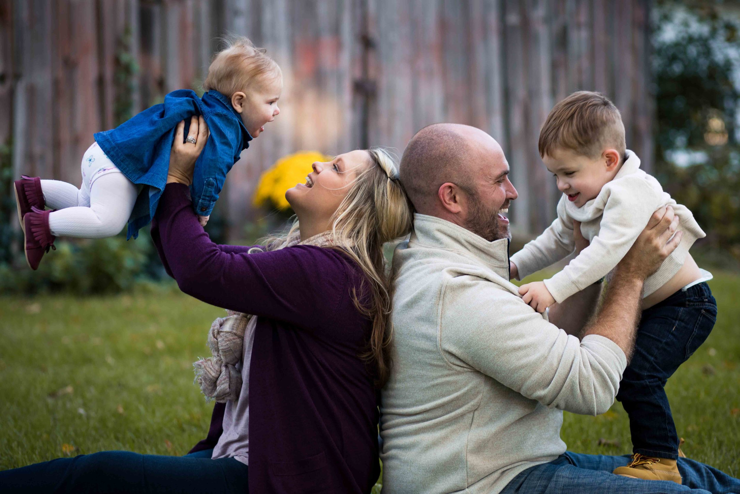  Mom and dad sit back to back each holding a child in the air 