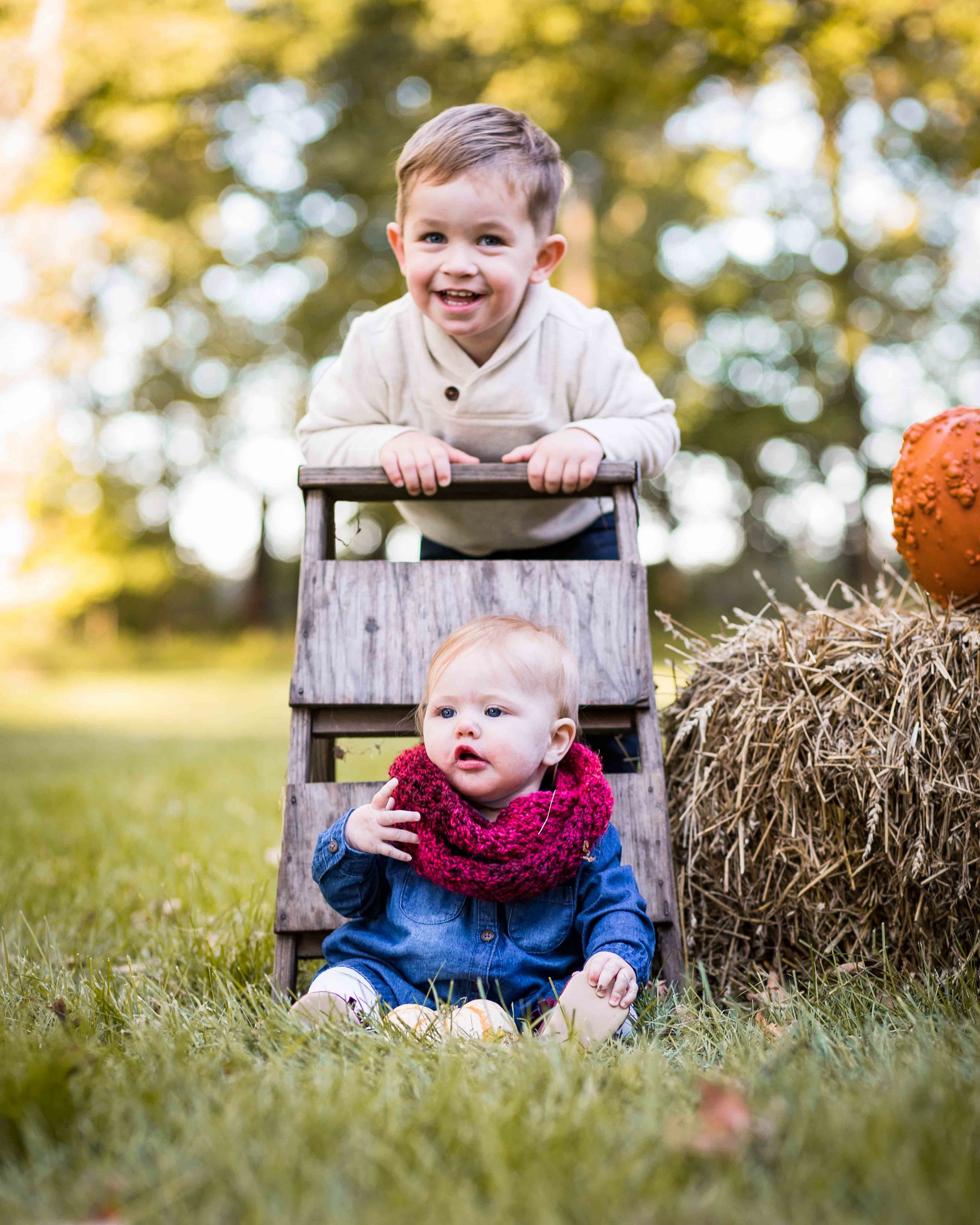  Siblings posing for a photo with a ladder, hay bales, and a pumpkin 