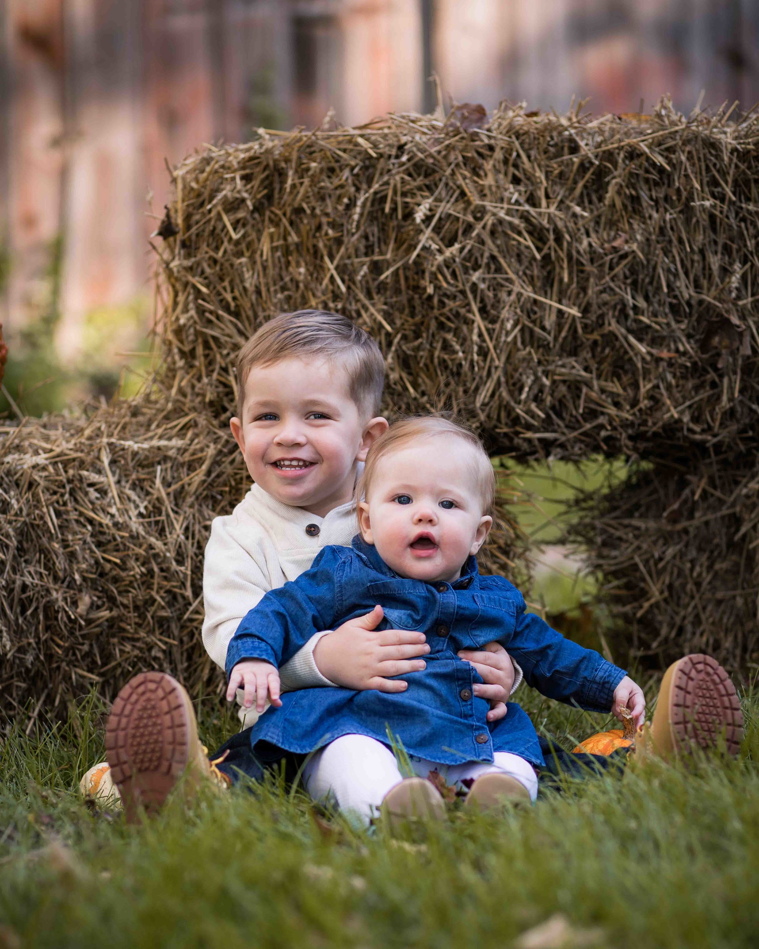  big brother holding his little sister in front of a hay bale at the Shiloh Farm barn in Richland, MI 