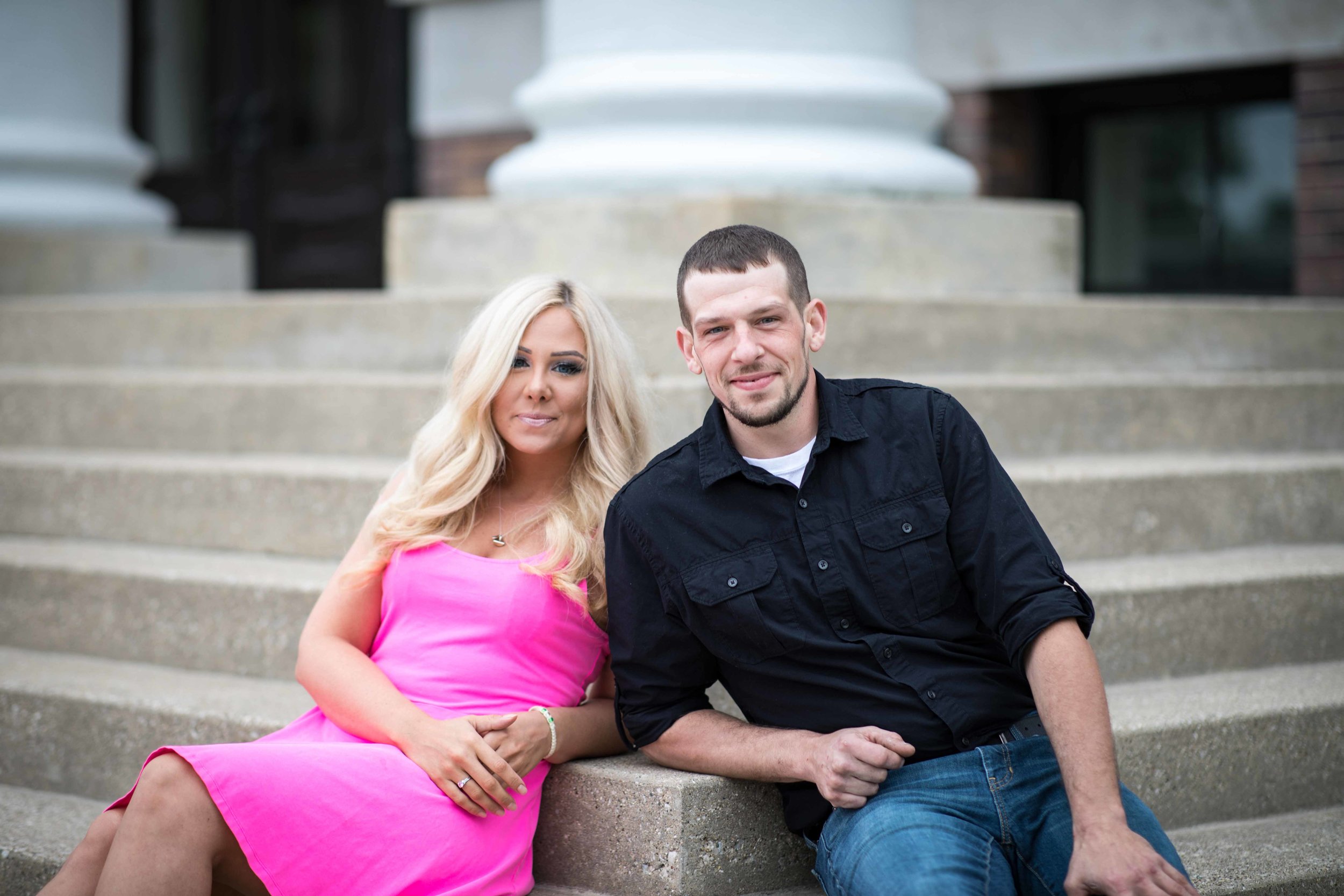  Engaged couple sitting on the steps of historic Heritage Hall in Kalamazoo 