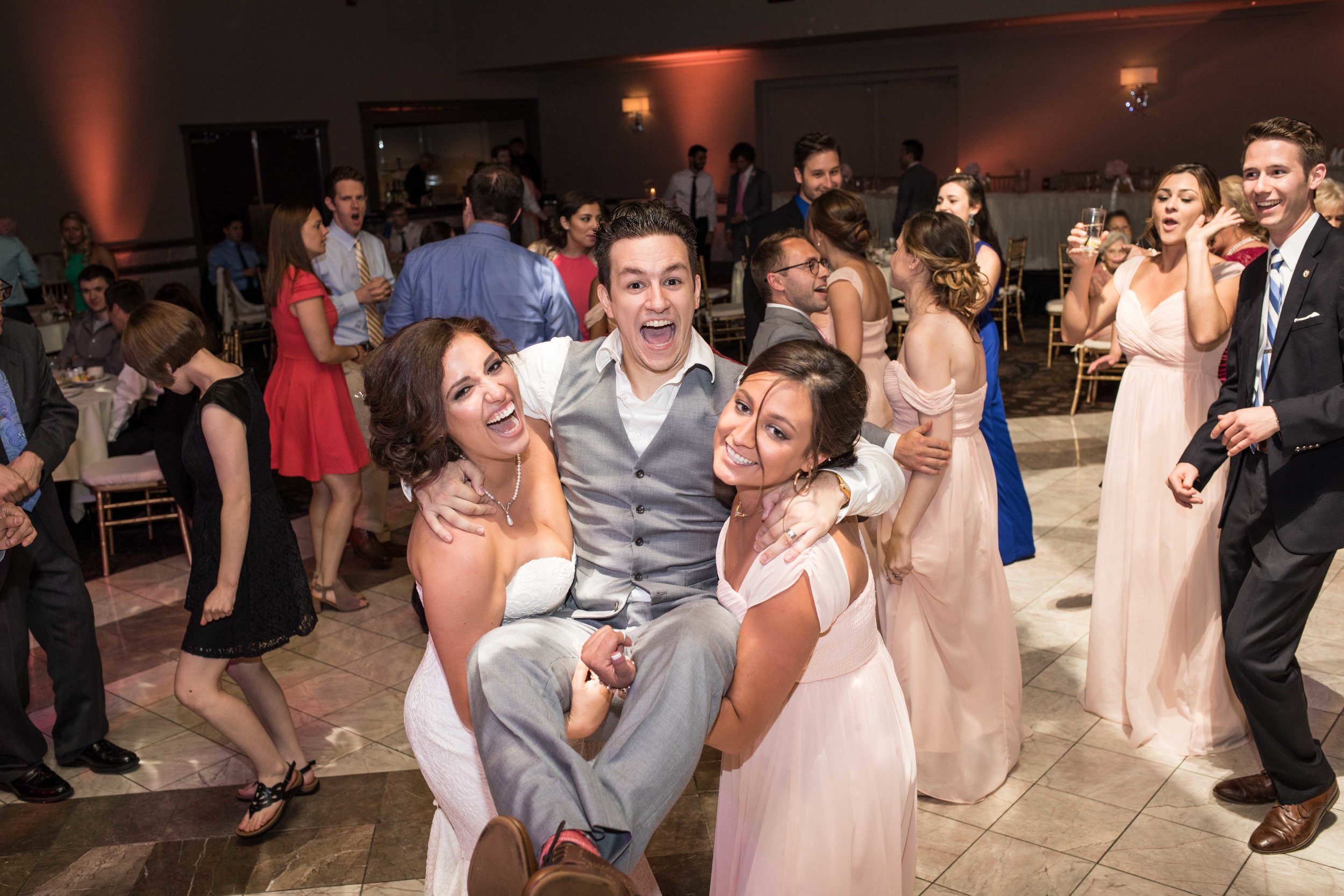  Bride and bridesmaid holding groom on the dance floor all laughing 