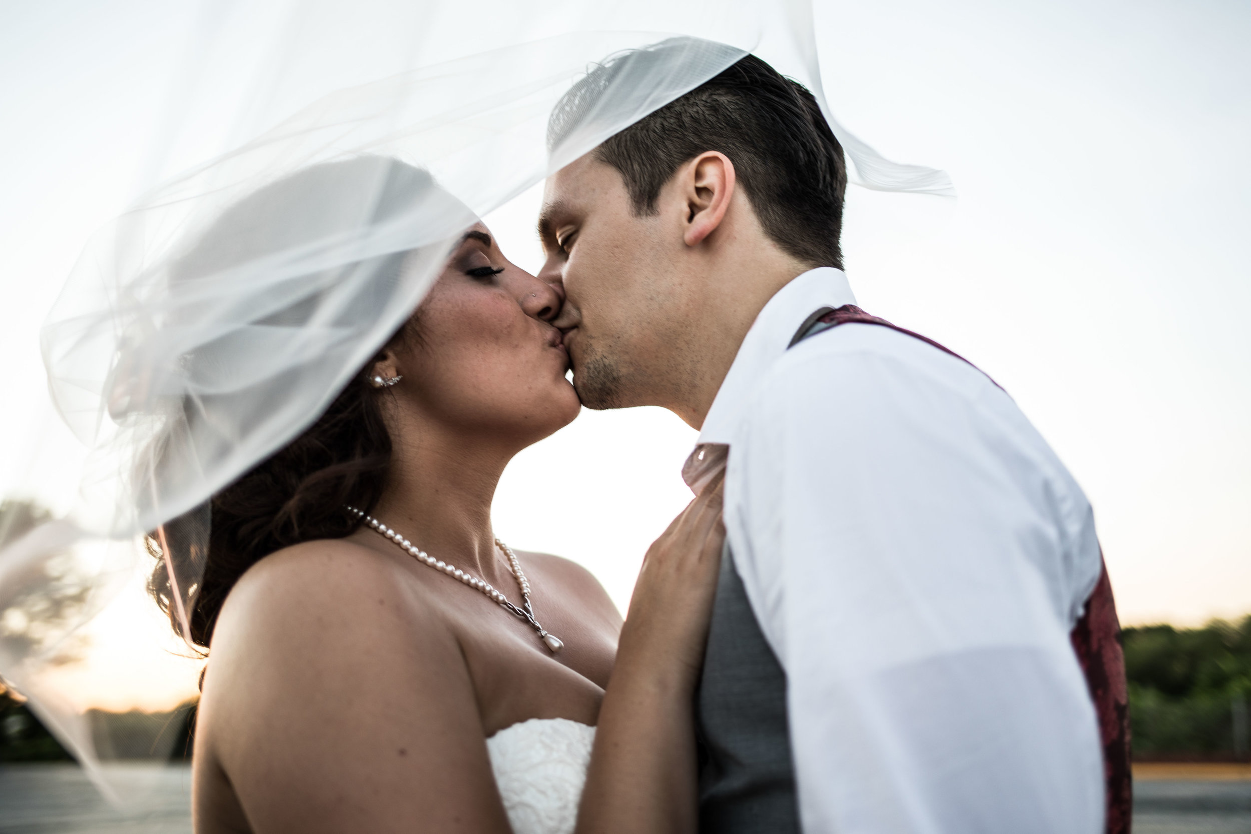  bride and groom kissing through wind blown veil 