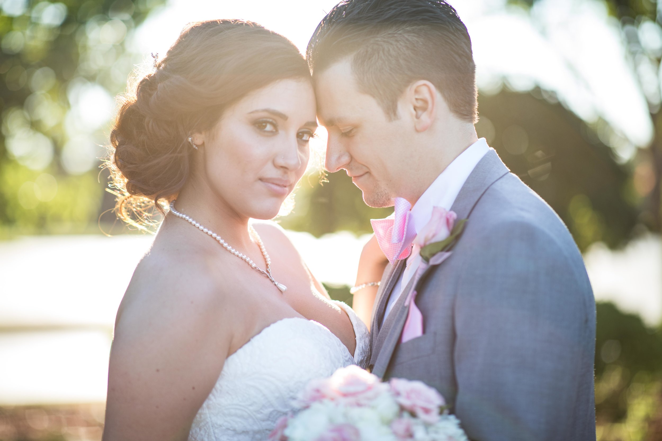  Bride looks directly at the photographer while the groom holds her close during sunset 