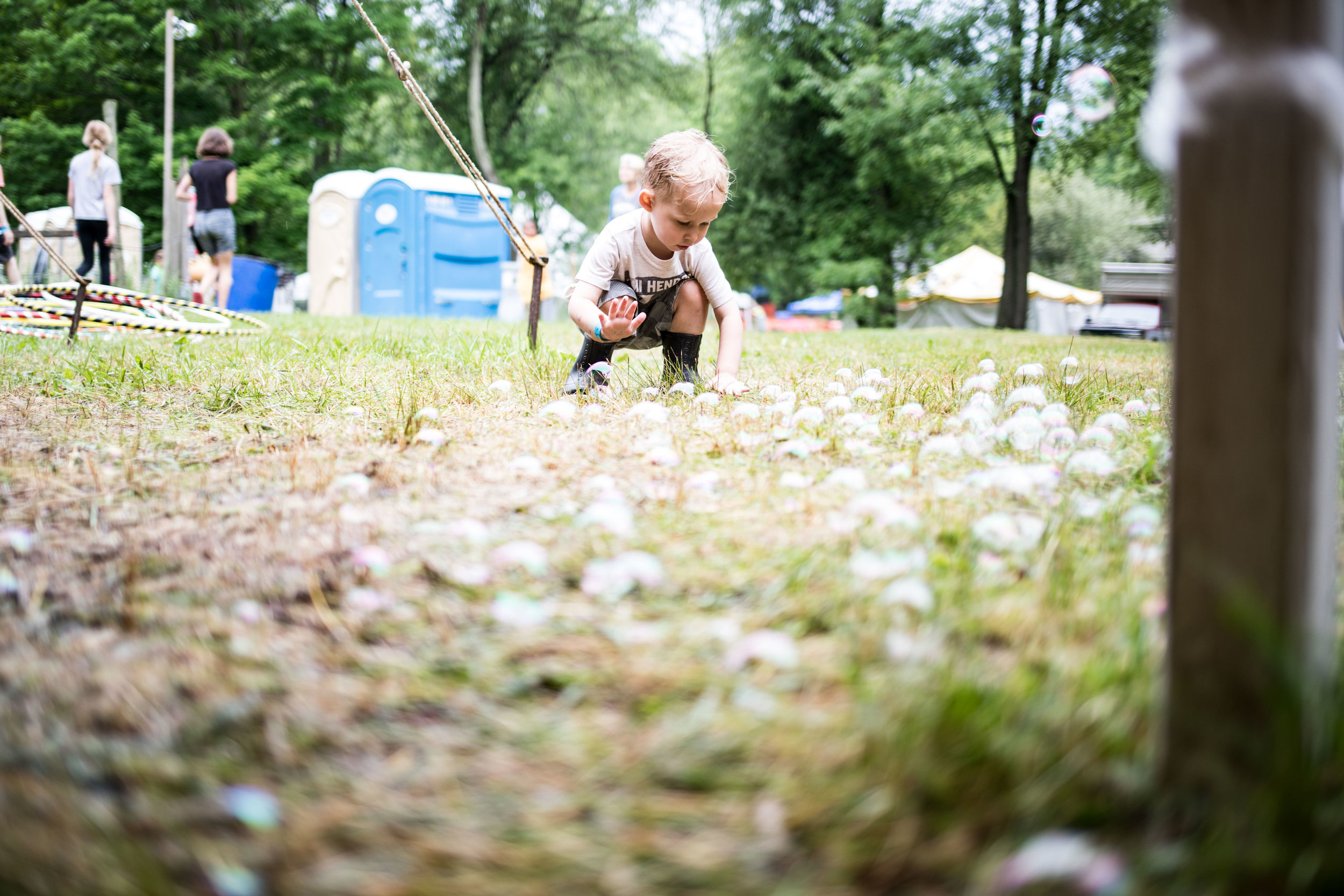  a small child popping bubbles which are scattered all over the ground in front of him 