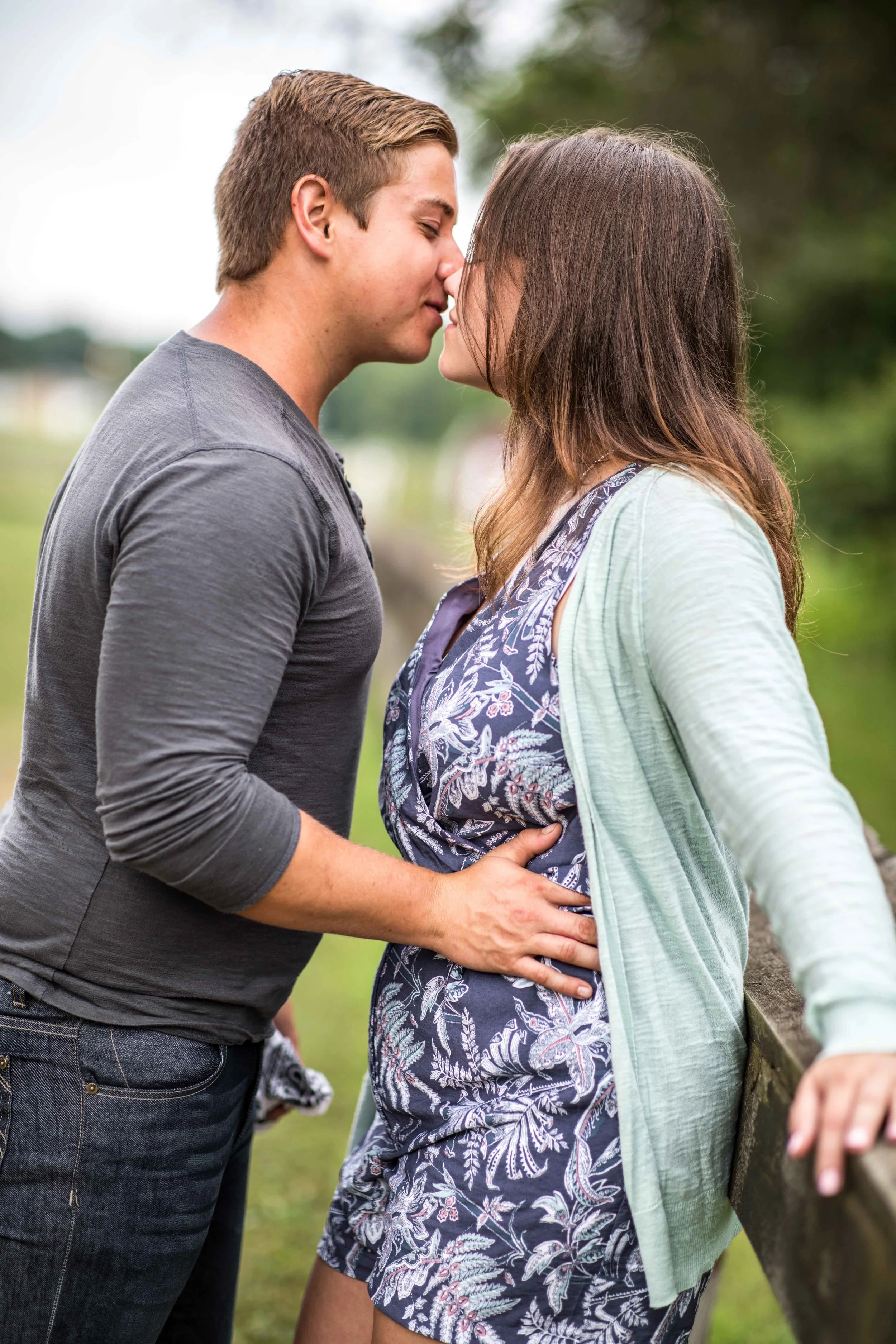 he presses against her for a kiss as she leans against a split rail fence