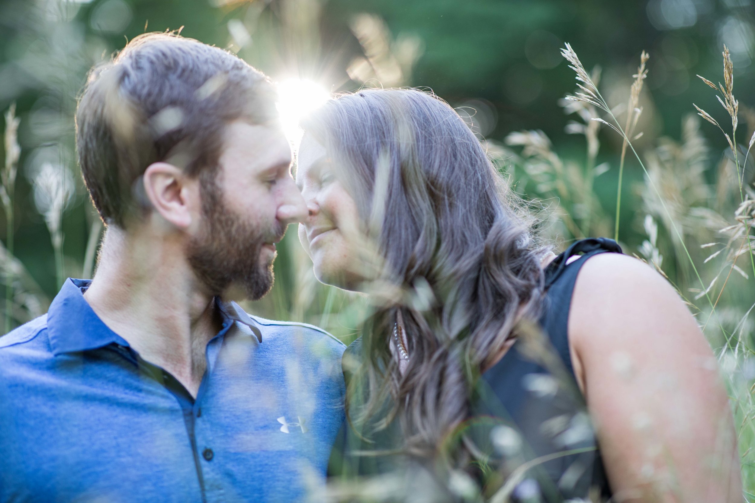  man and woman kissing in tall field grass behind a setting sun 