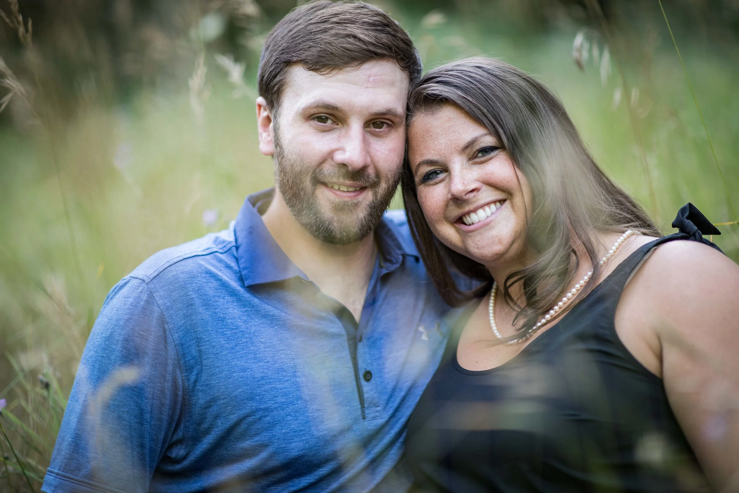man and woman leaning they’re heads together in a field of tall grass