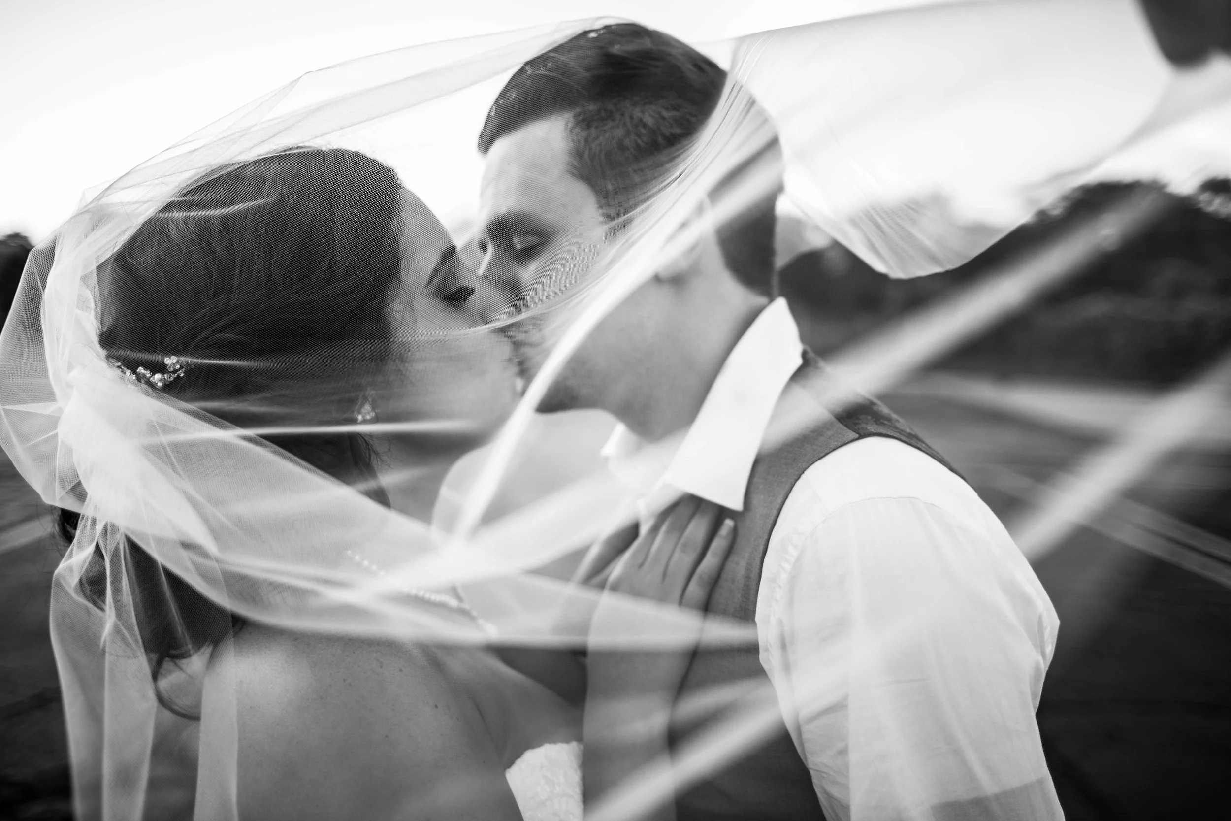 Black and white bride and groom kissing through wind blown veil.jpg