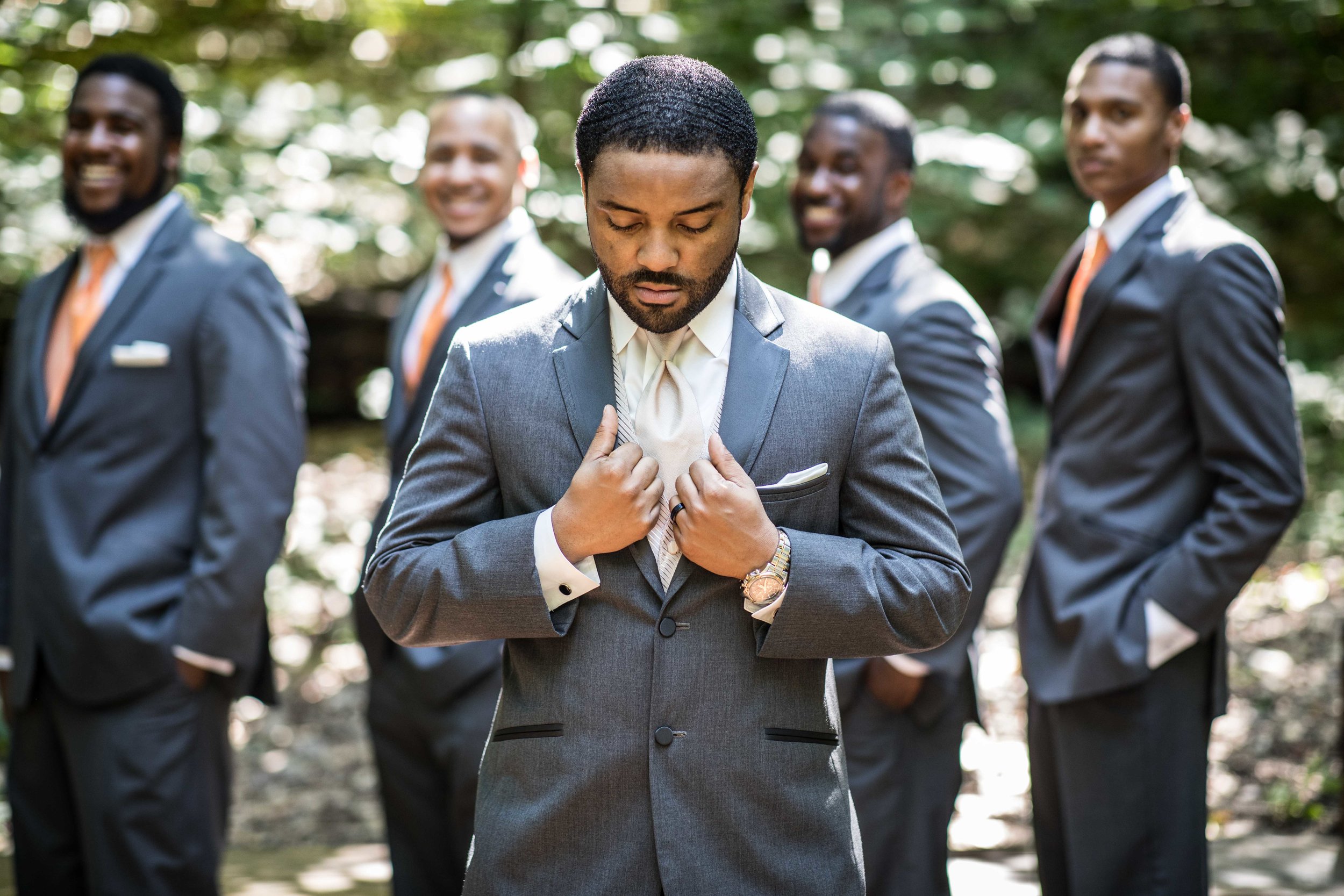  The groom straightening his suit with groomsmen lined up behind him 