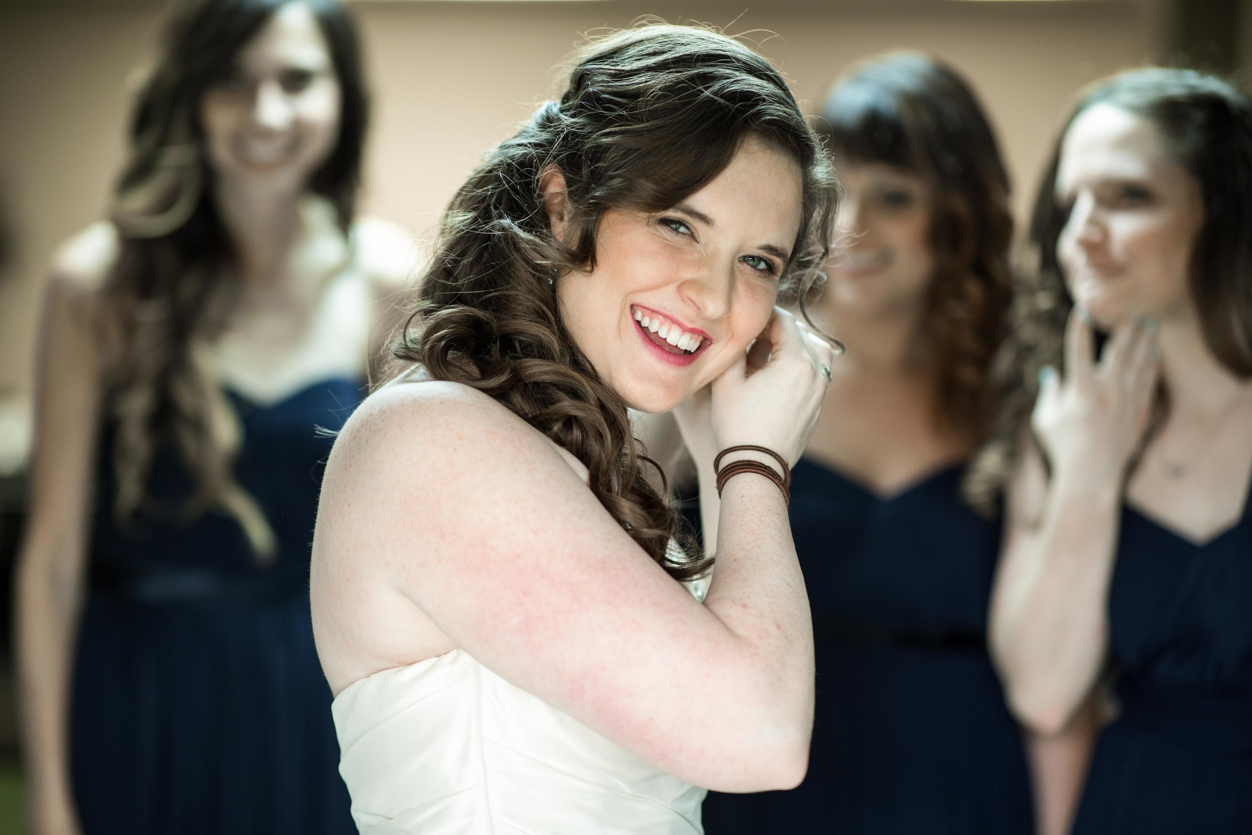  The bride putting in earrings with bridesmaids behind her 