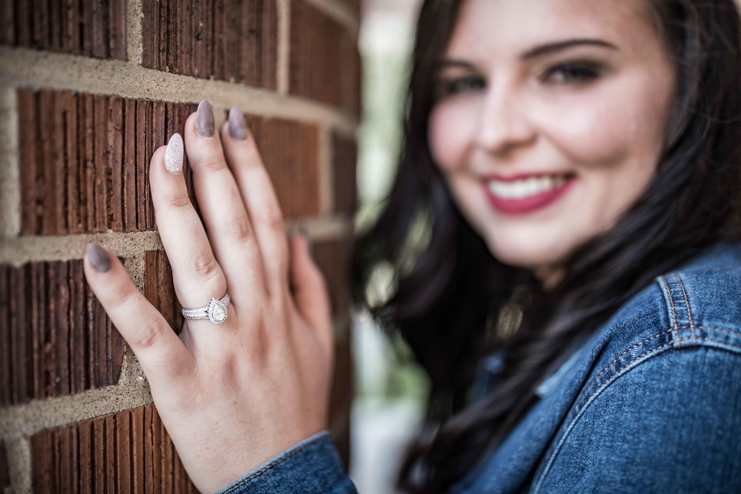  she shows off her engagement ring against a brick pillar 