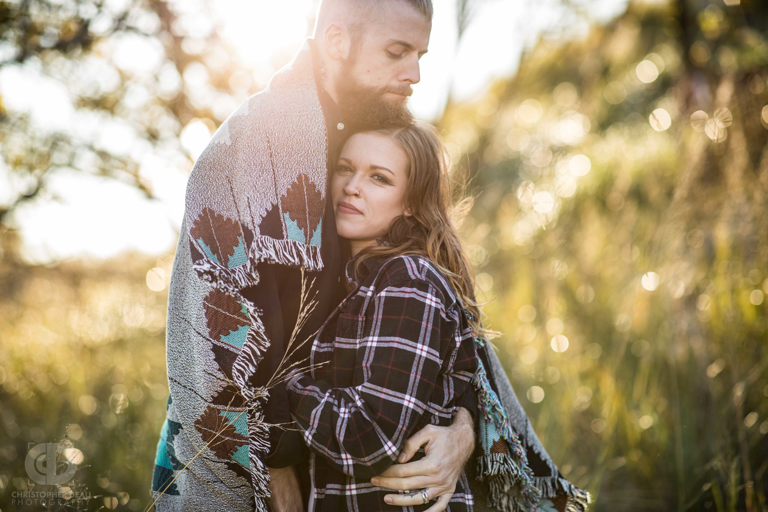  couple embrace, wrapped in blanket with sunset in background 