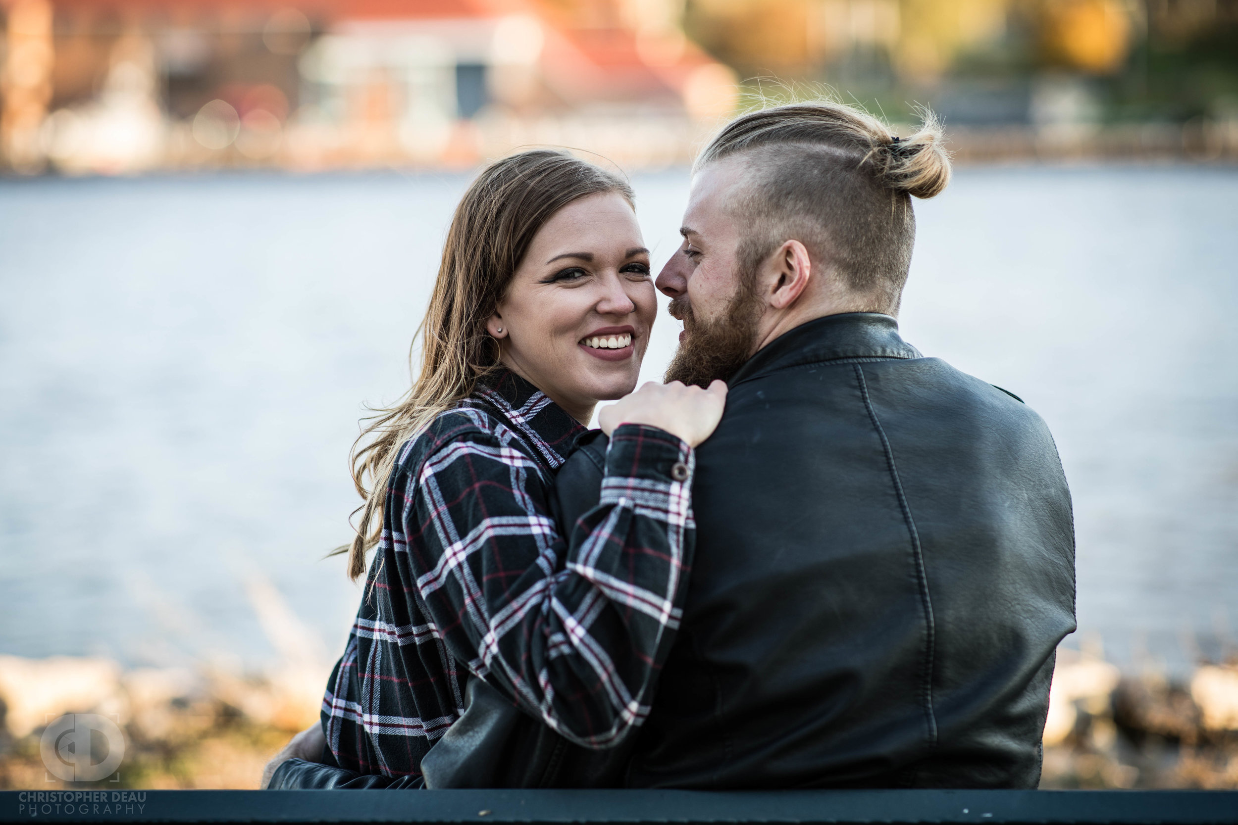  An engaged couple sits on a bench in front of the Grand River in Michigan 