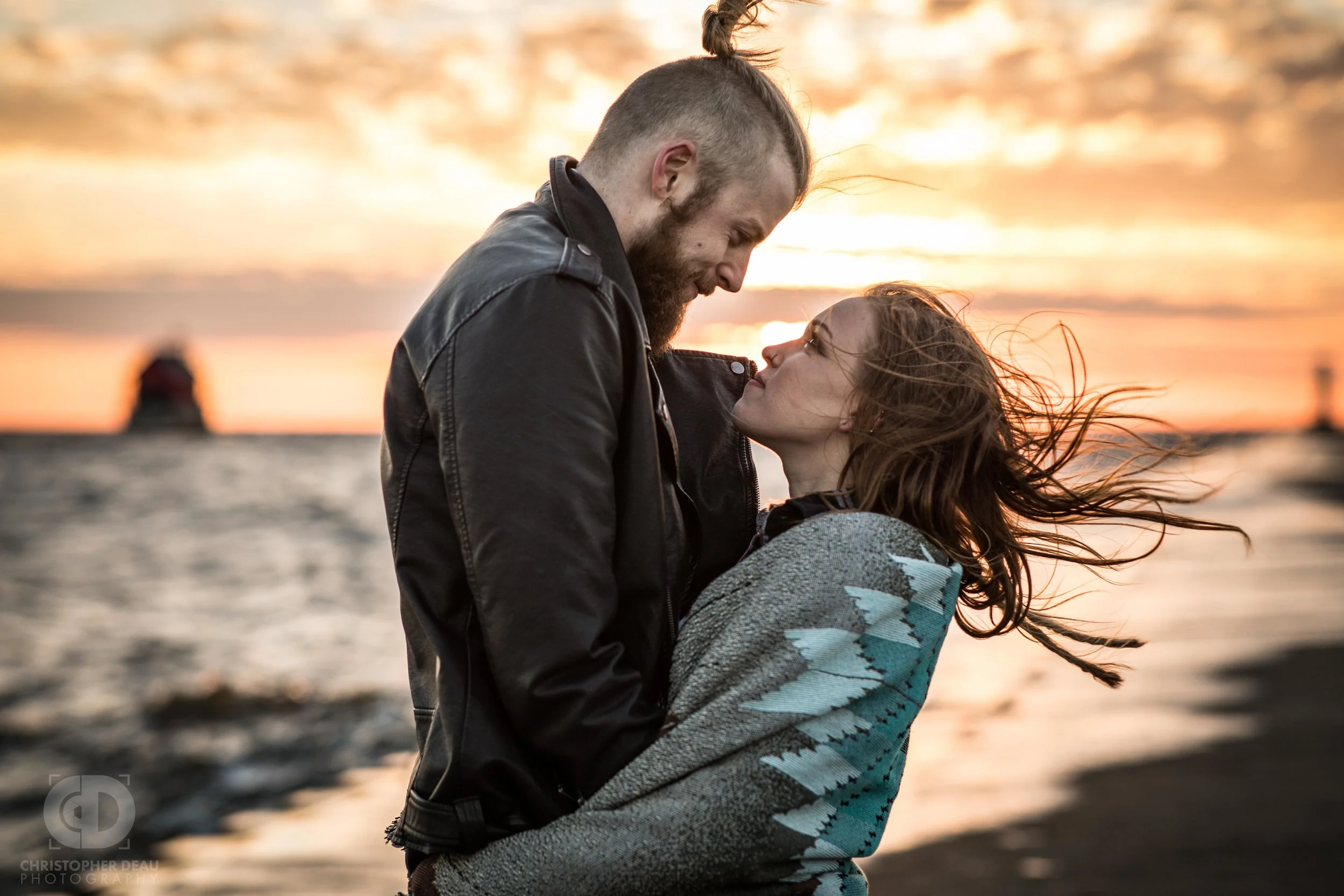 wind blowing couples hair in front of a sunset on a pier in Grand Haven, Michigan
