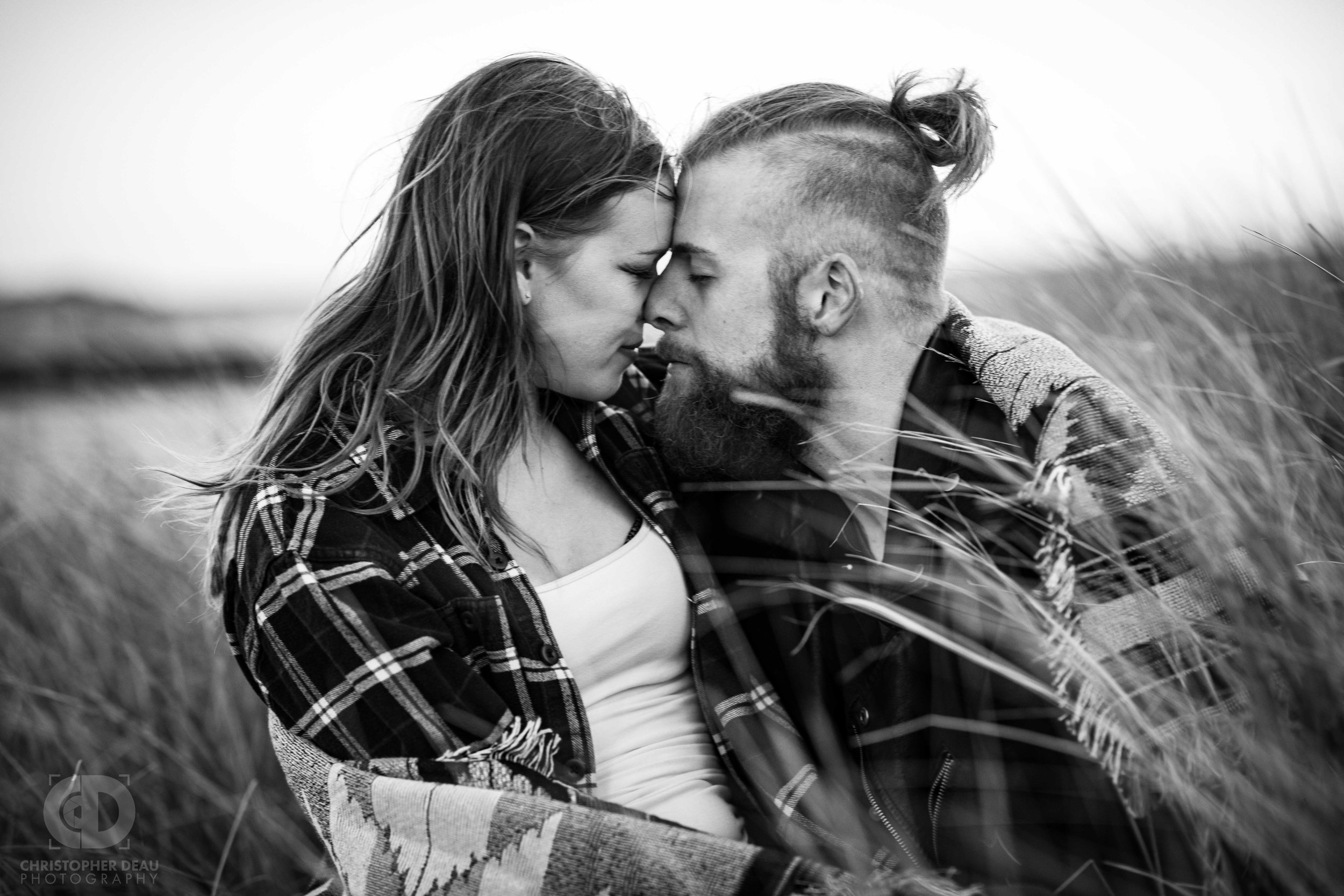  A couple snuggles in a warm blanket sitting in dune grass on a Lake Michigan Beach in Autumn  