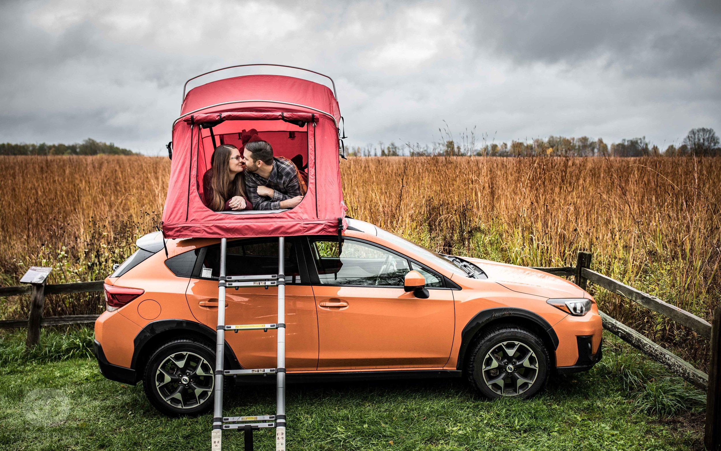  a couple takes their engagement photos in their Subaru Crosstrek roof tent while parked in an open tall grass prairie 