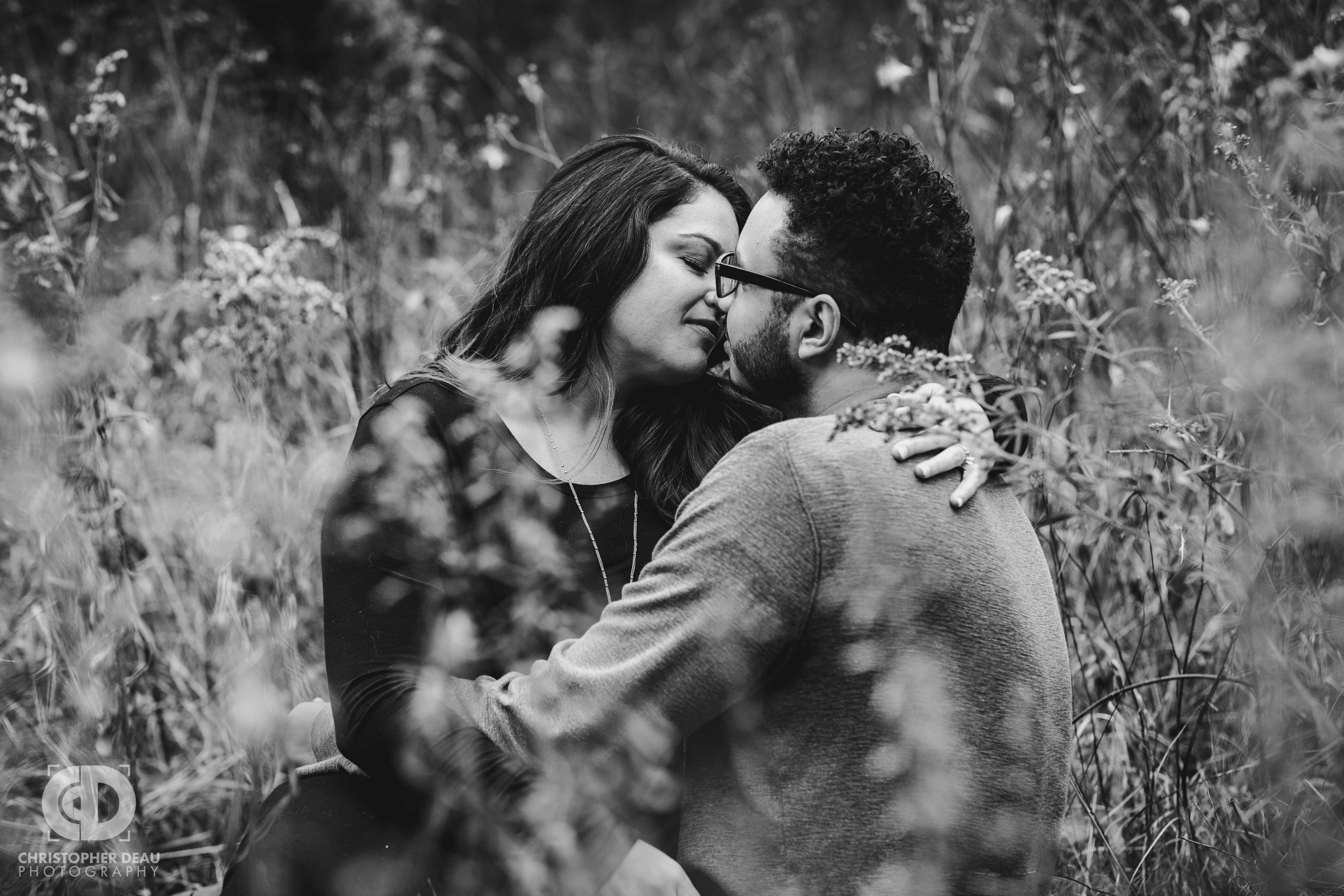  black and white image of man and woman sitting in a tall grass prairie for engagement photos in Kalamazoo Michigan 