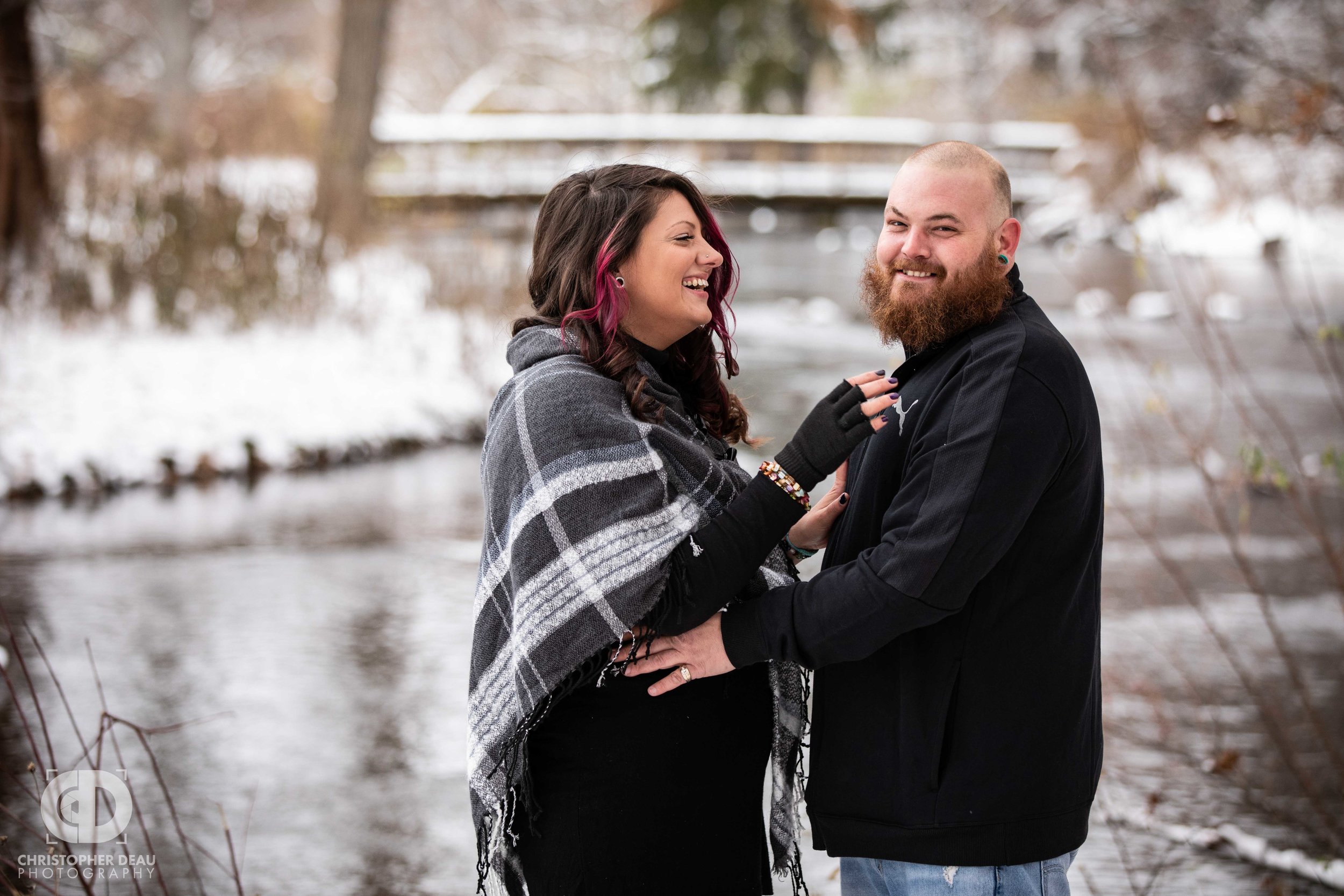  man and woman laughing in front of a stream and bridge in a southwest Michigan Park for their engagement photos 