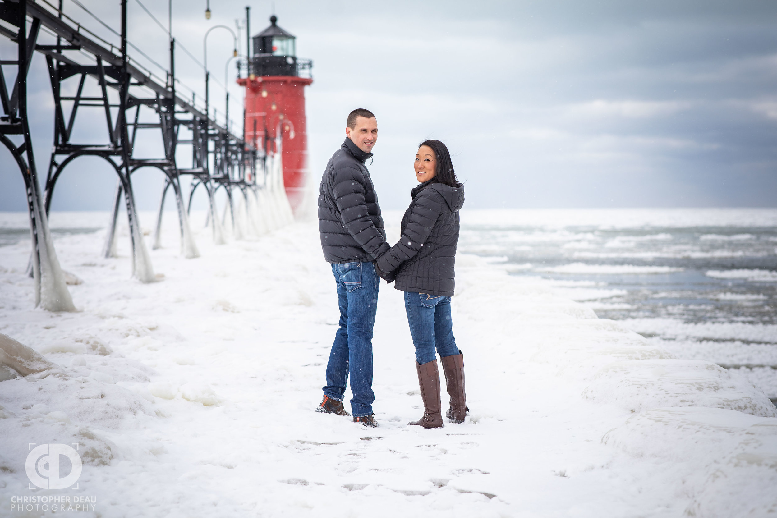  couple holding hands walking down south haven lighthouse pier during engagement session 