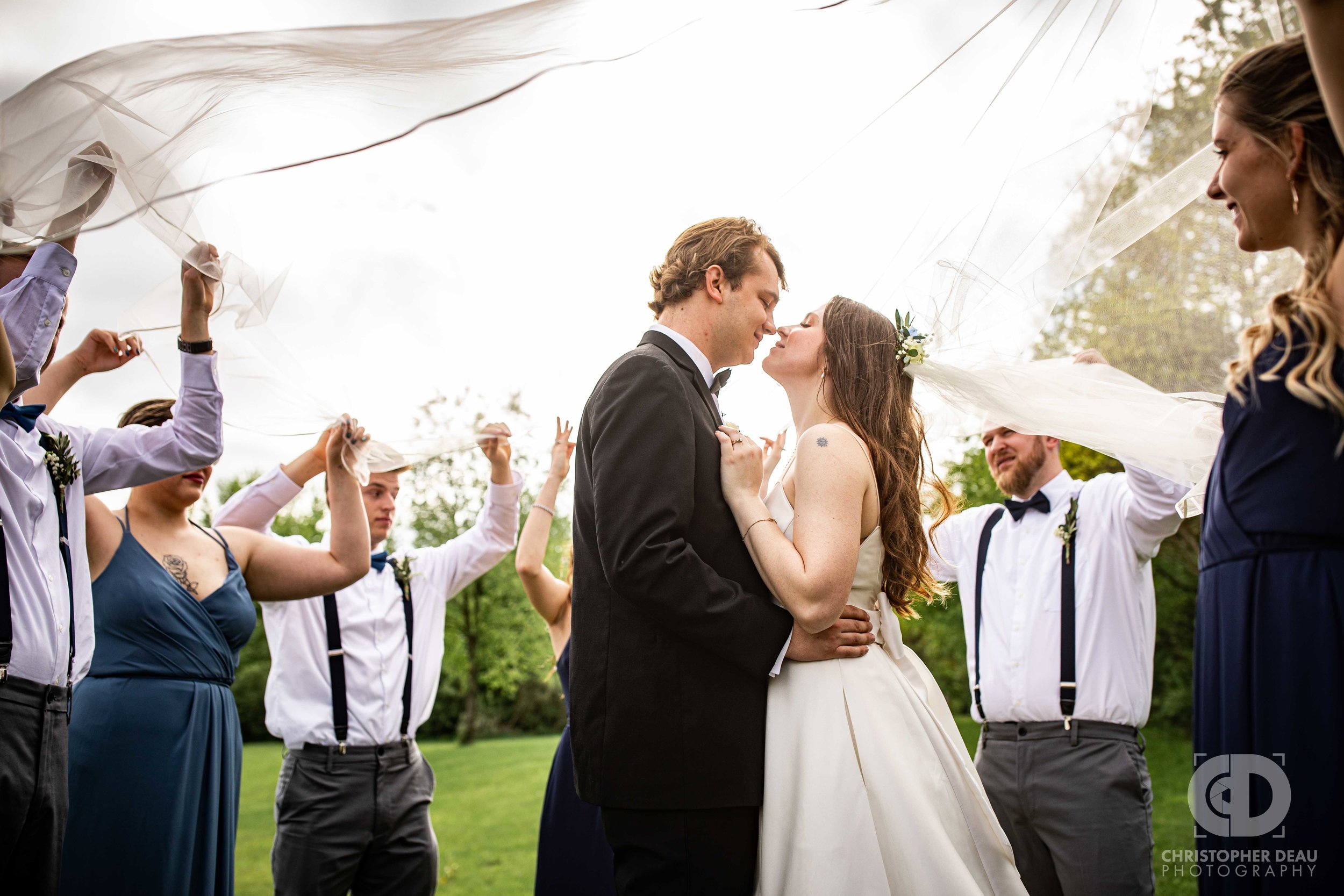  wedding party holds veil up around bride and groom 