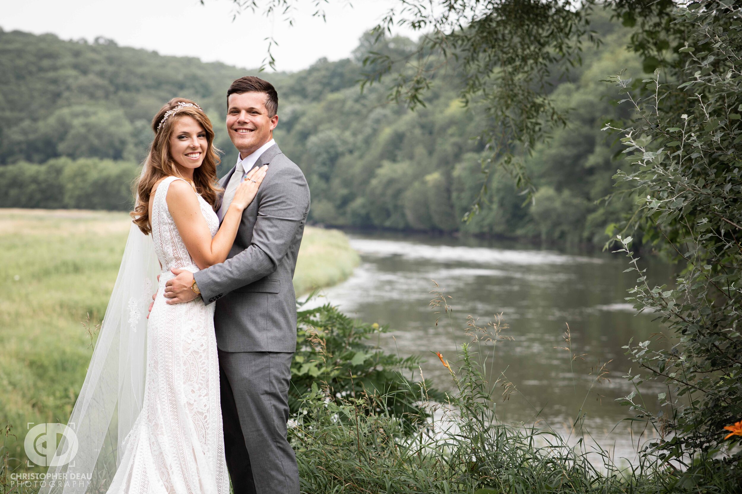  bride and groom pose for the wedding photographer in front of a beautiful field and flowing river. 