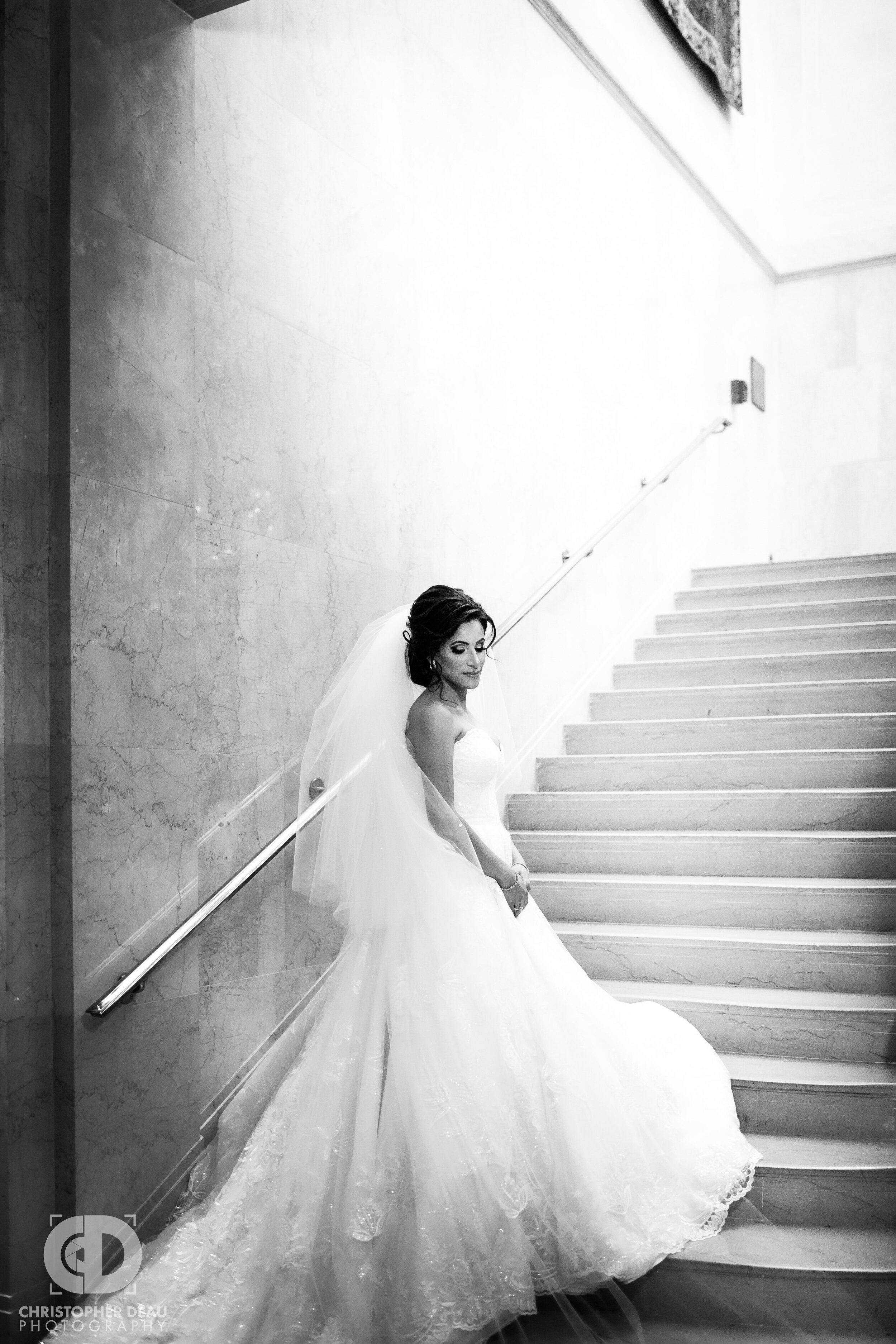  black and white image of a bride in a white dress flowing down a staircase 