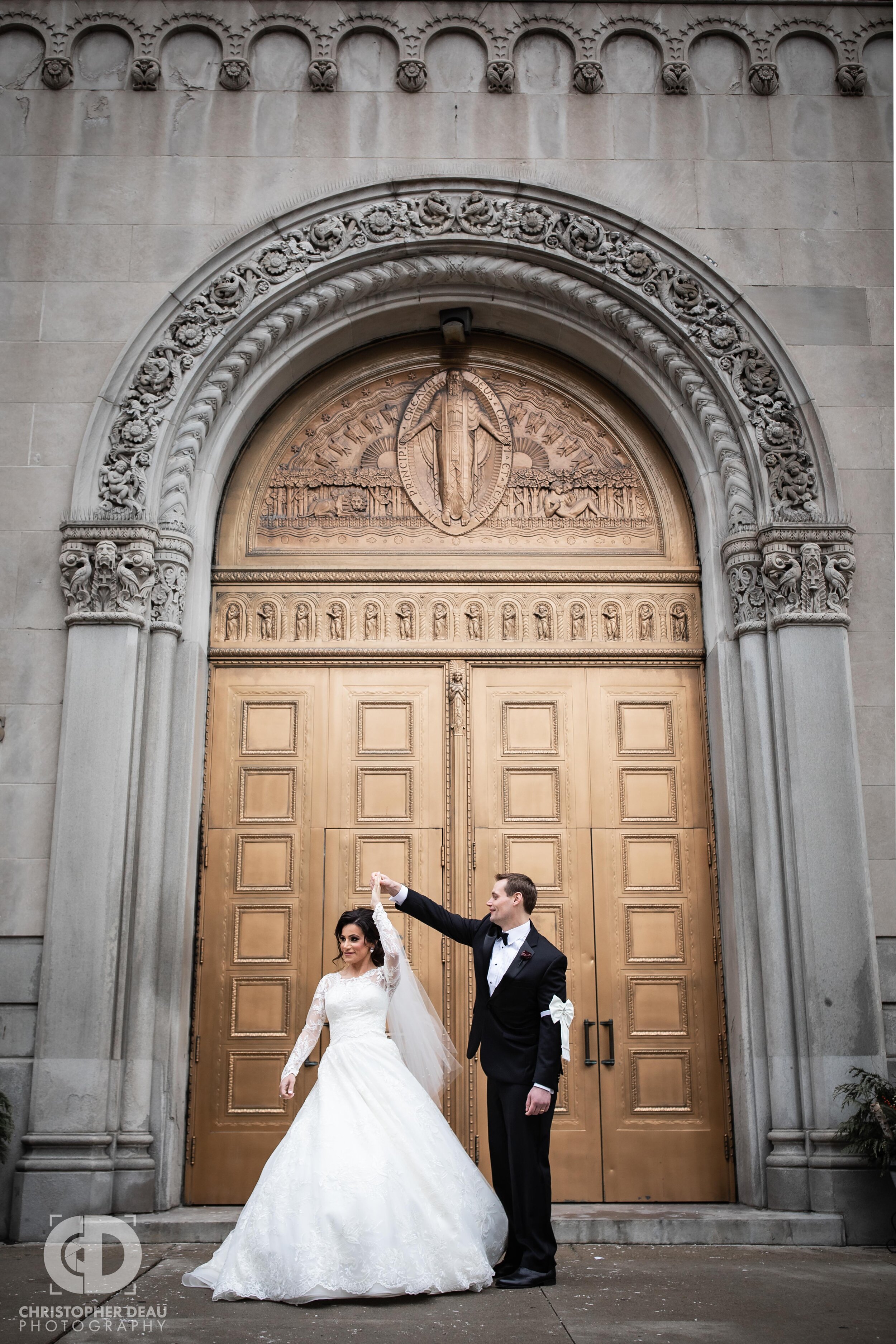  The groom spins the bride in front of the giant gold doors of St Aloysius Parish in Detroit Michigan 