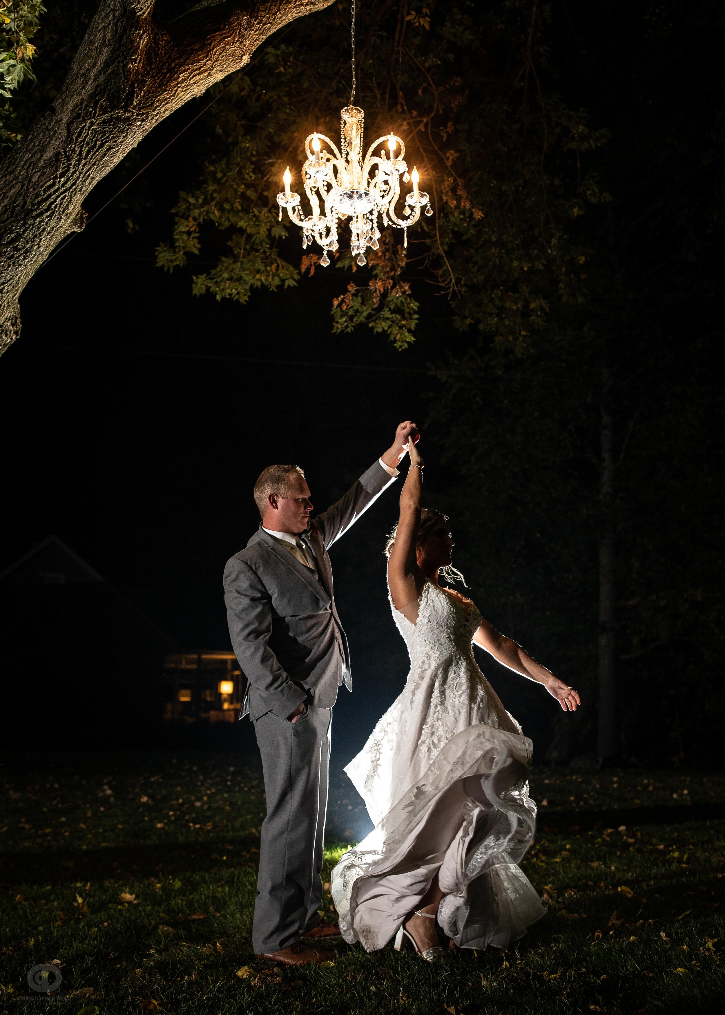  bride and groom twirl under chandelier in the dark 