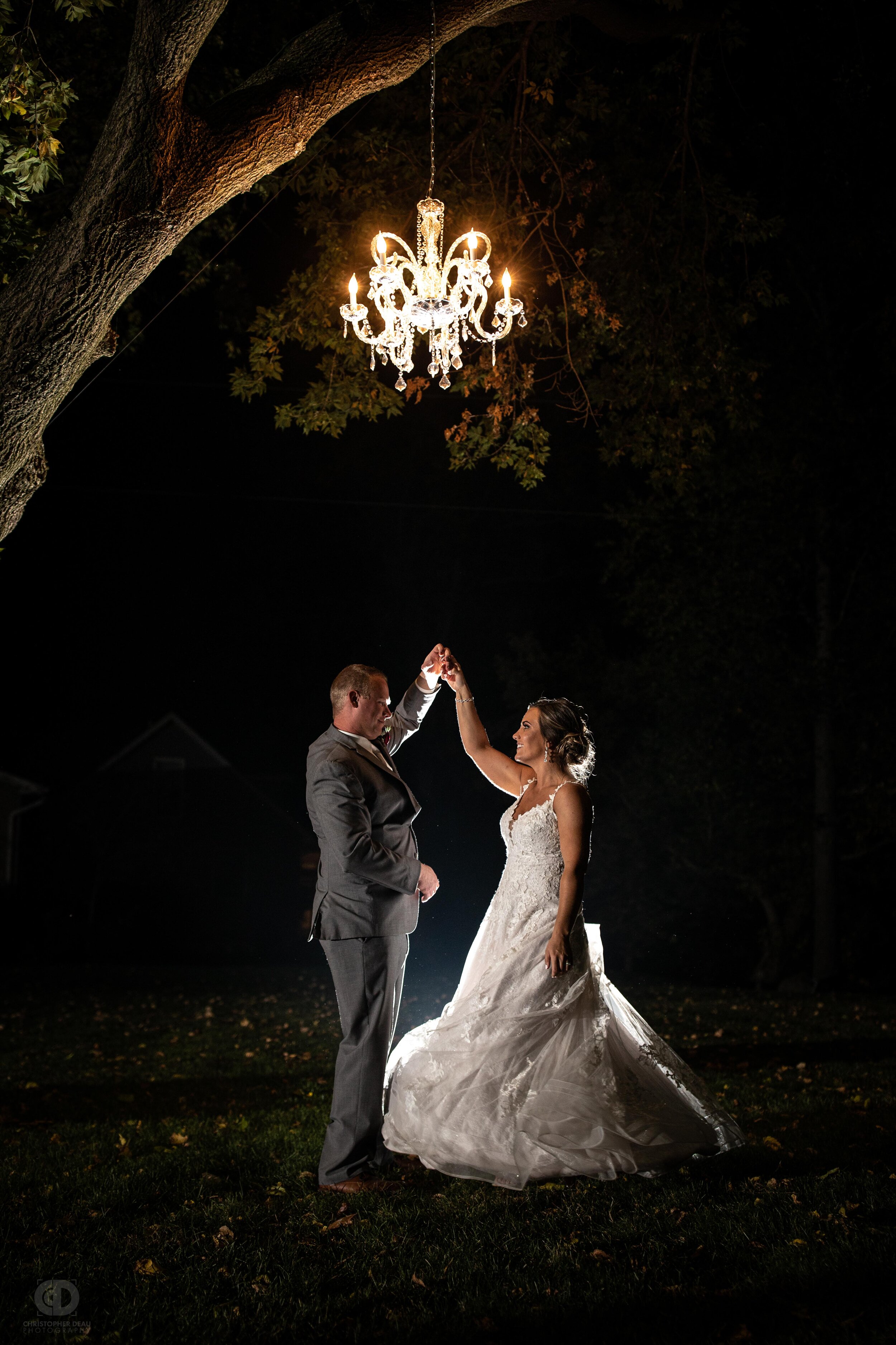  bride and groom twirl under chandelier in the dark 