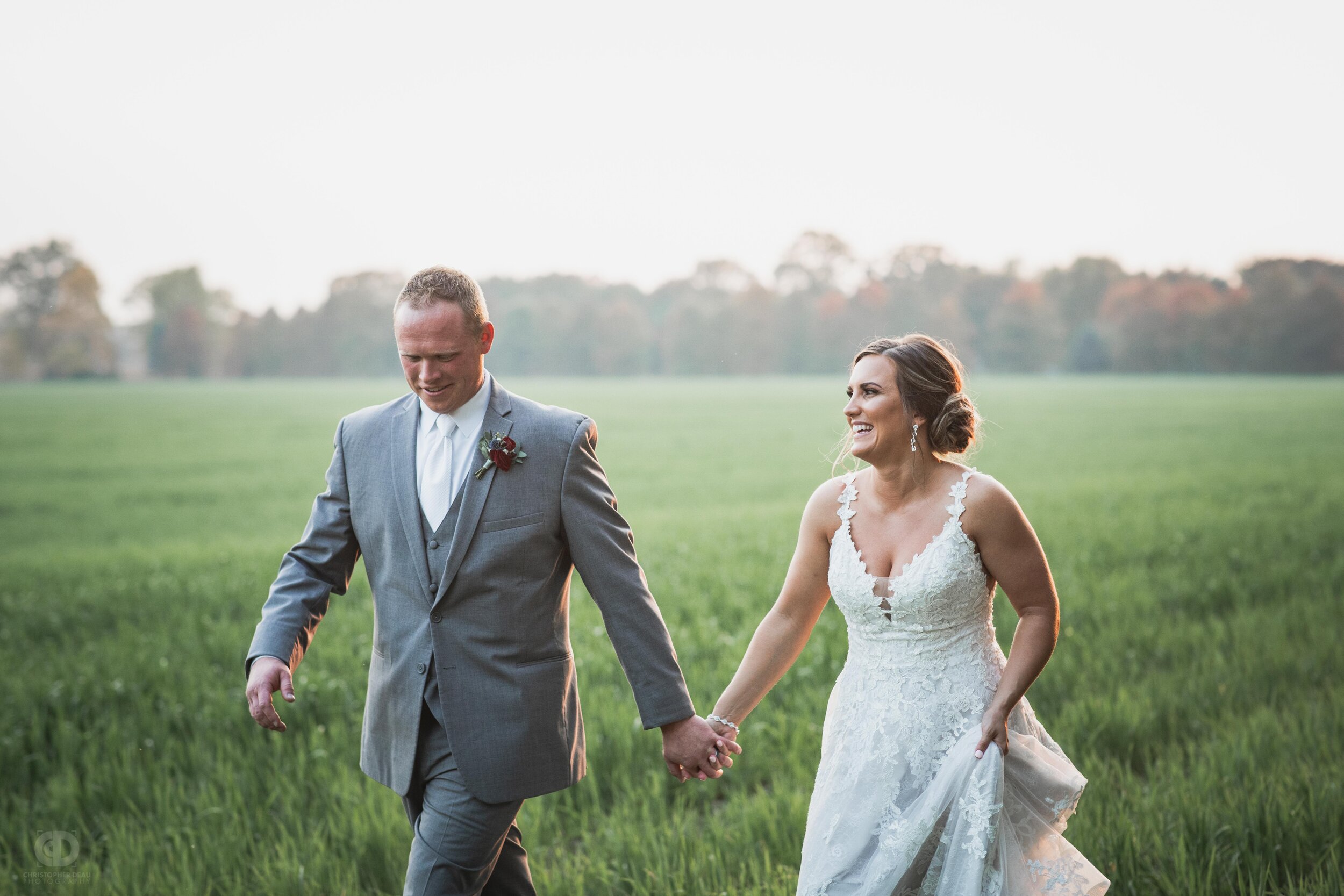  bride and groom walk through green field during sunset on their wedding day 