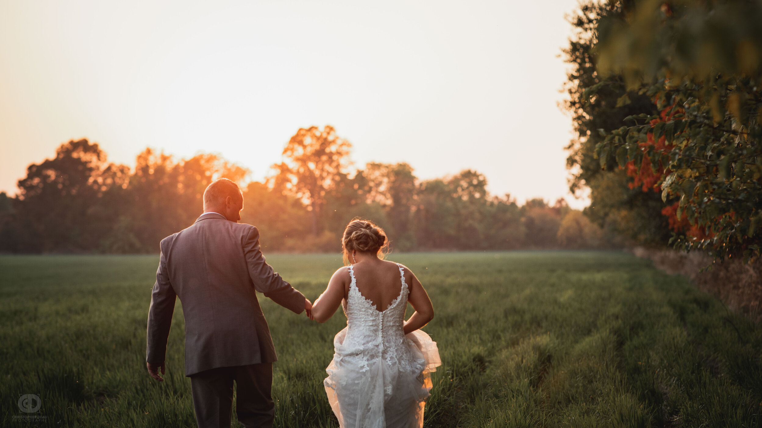  bride and groom walking toward sunset in a field 