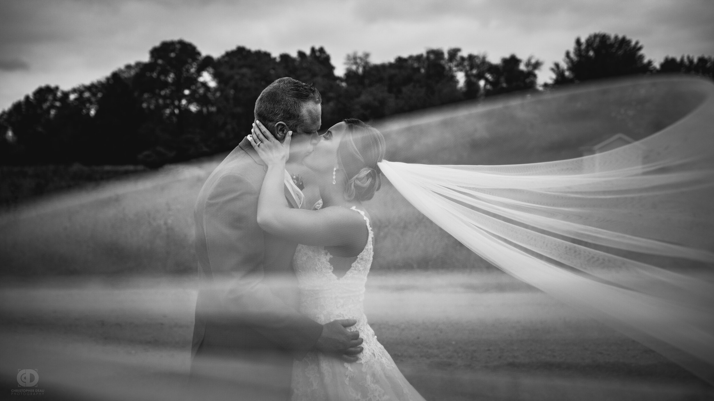  bride and groom kiss with wind blowing the brides veil black and white 
