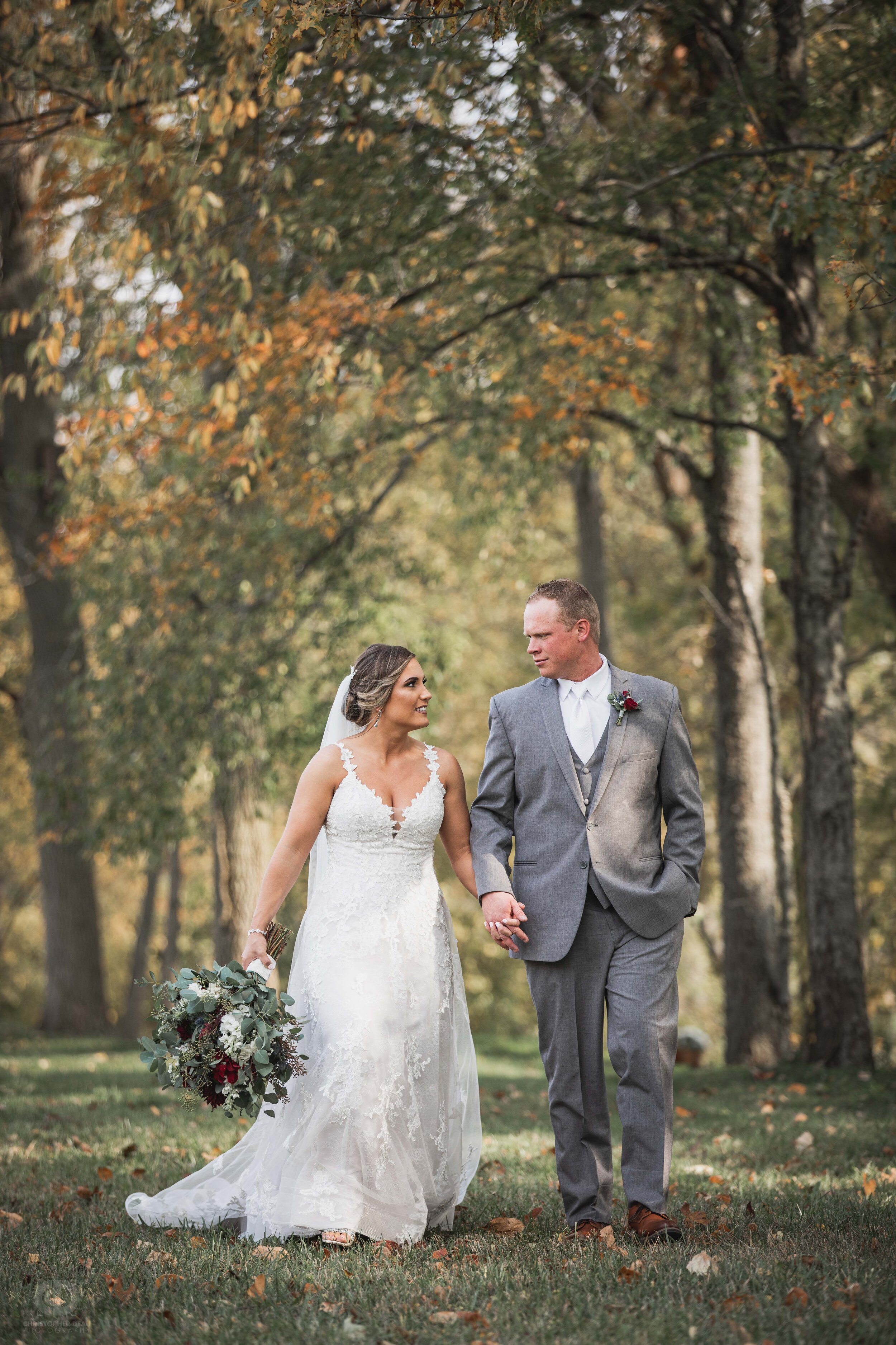  bride and groom walking together under fall leaves 