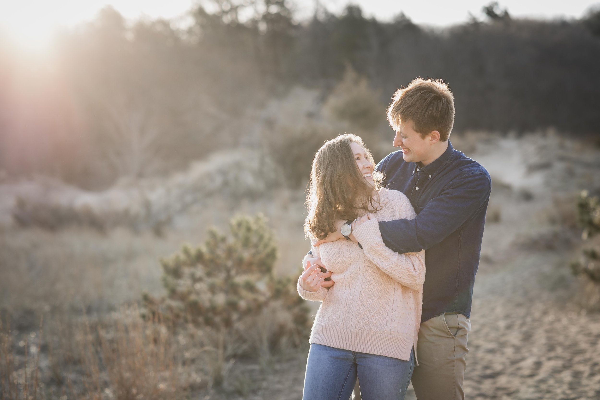  A couple playfully hugging in beach grass during sunrise 