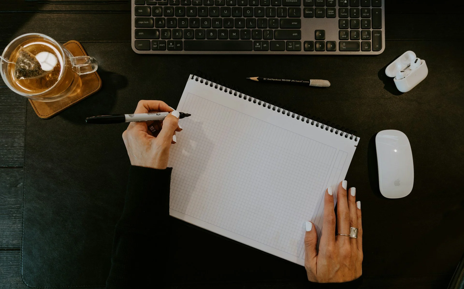 A top down image of someone's desk, with a person writing in a notepad.