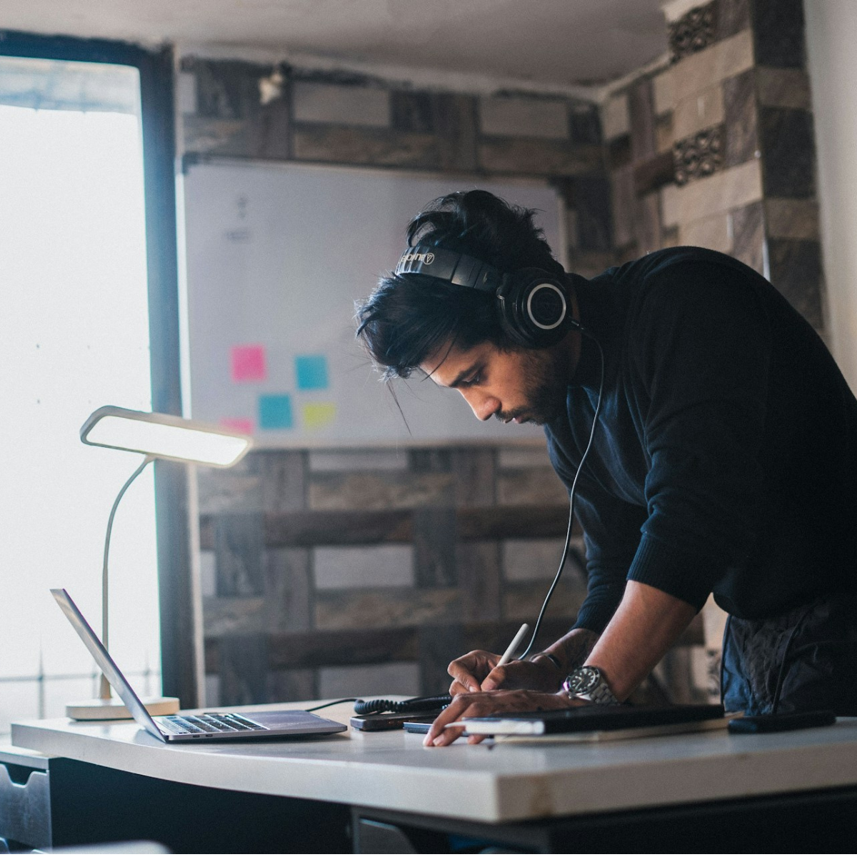 A photo of someone working at his desk listening to music through his headphones.