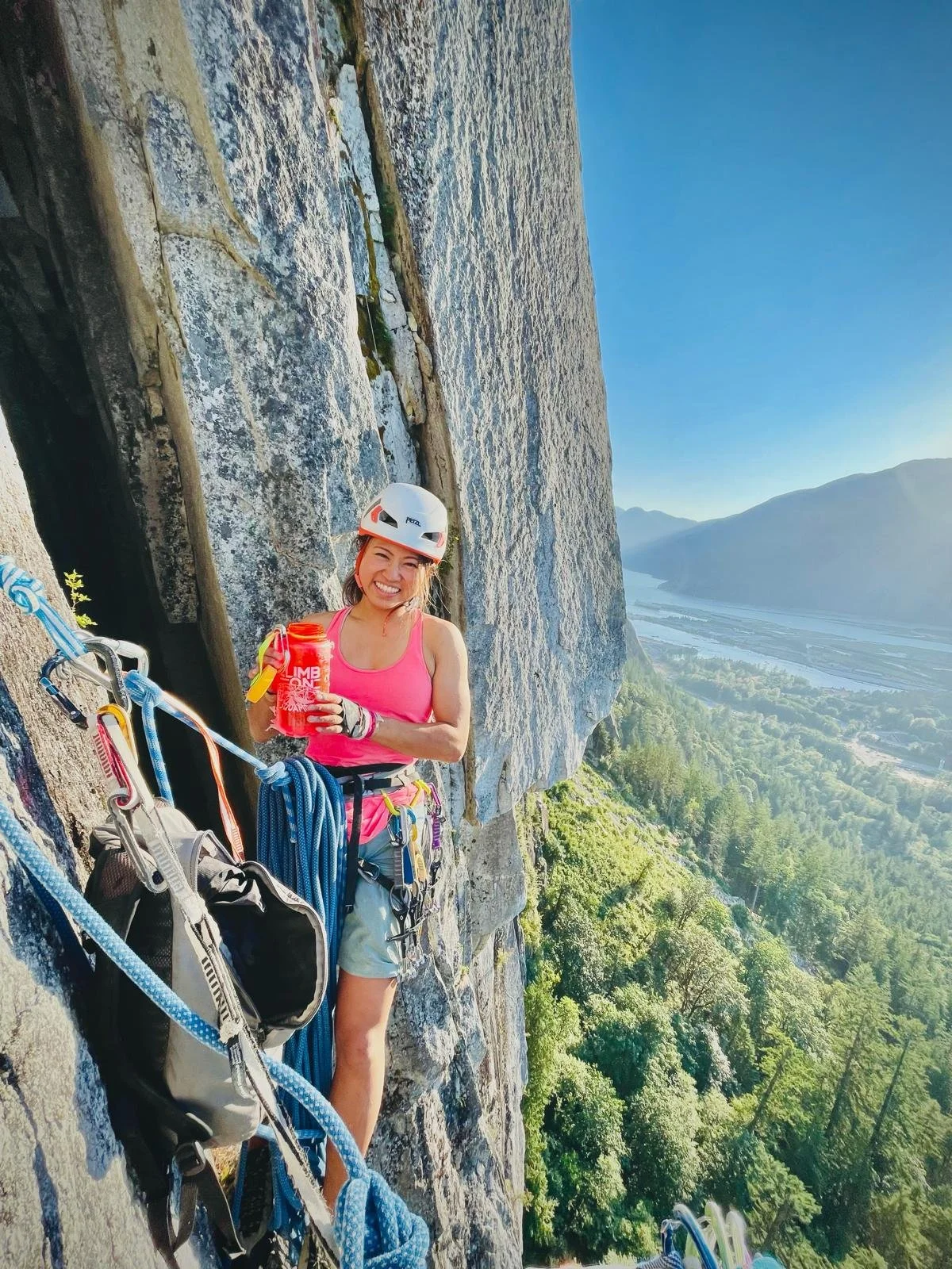 A woman is taking a break on the side of a steep cliff with climbing gear