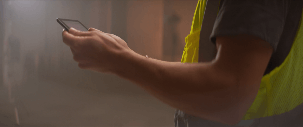Close-up of a construction worker using a tablet on-site, wearing a high-visibility safety vest, showcasing modern technology integration in industrial and engineering workflows.